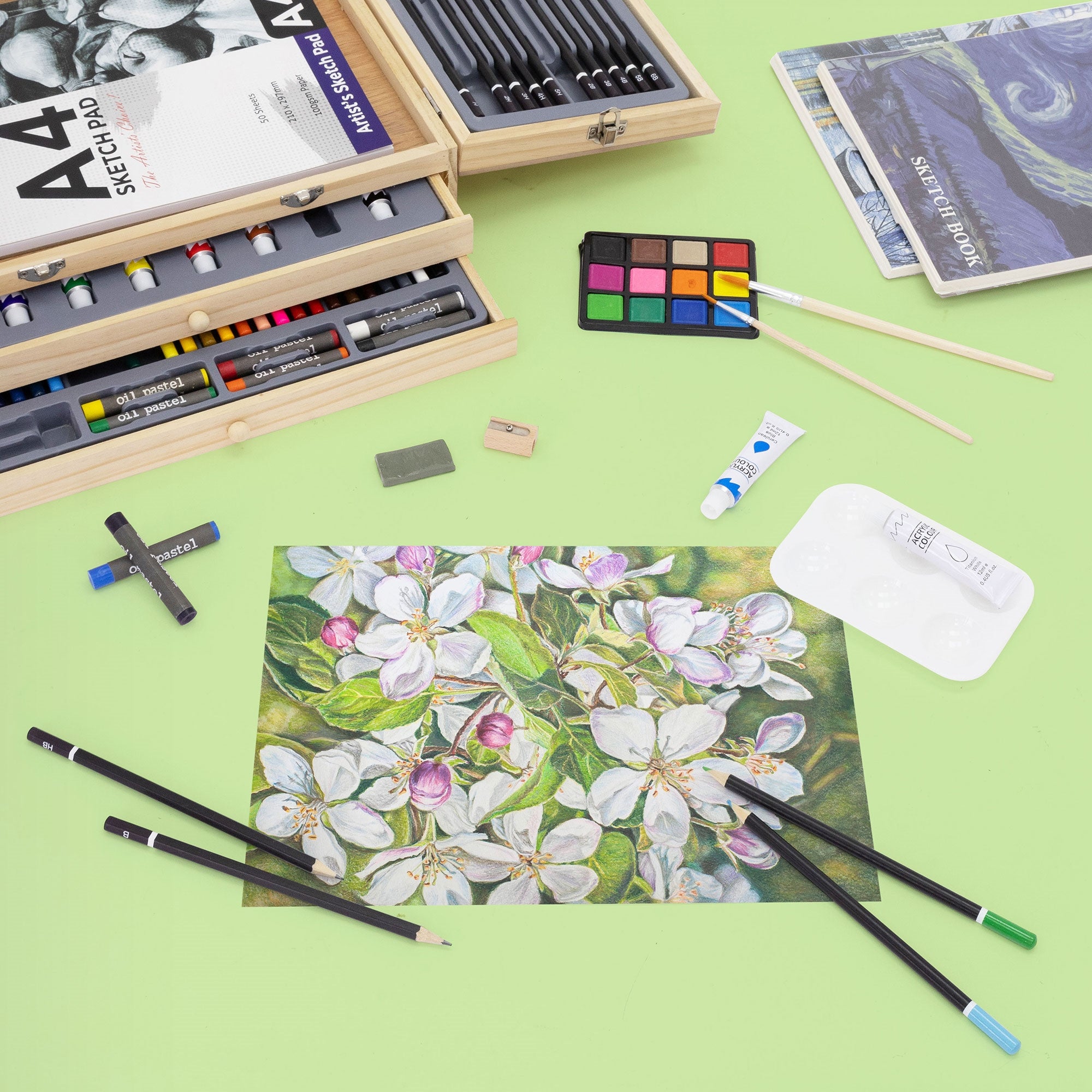 Kunstmaterialien und ein gemaltes Bild mit Blüten auf einem grünen Tisch.