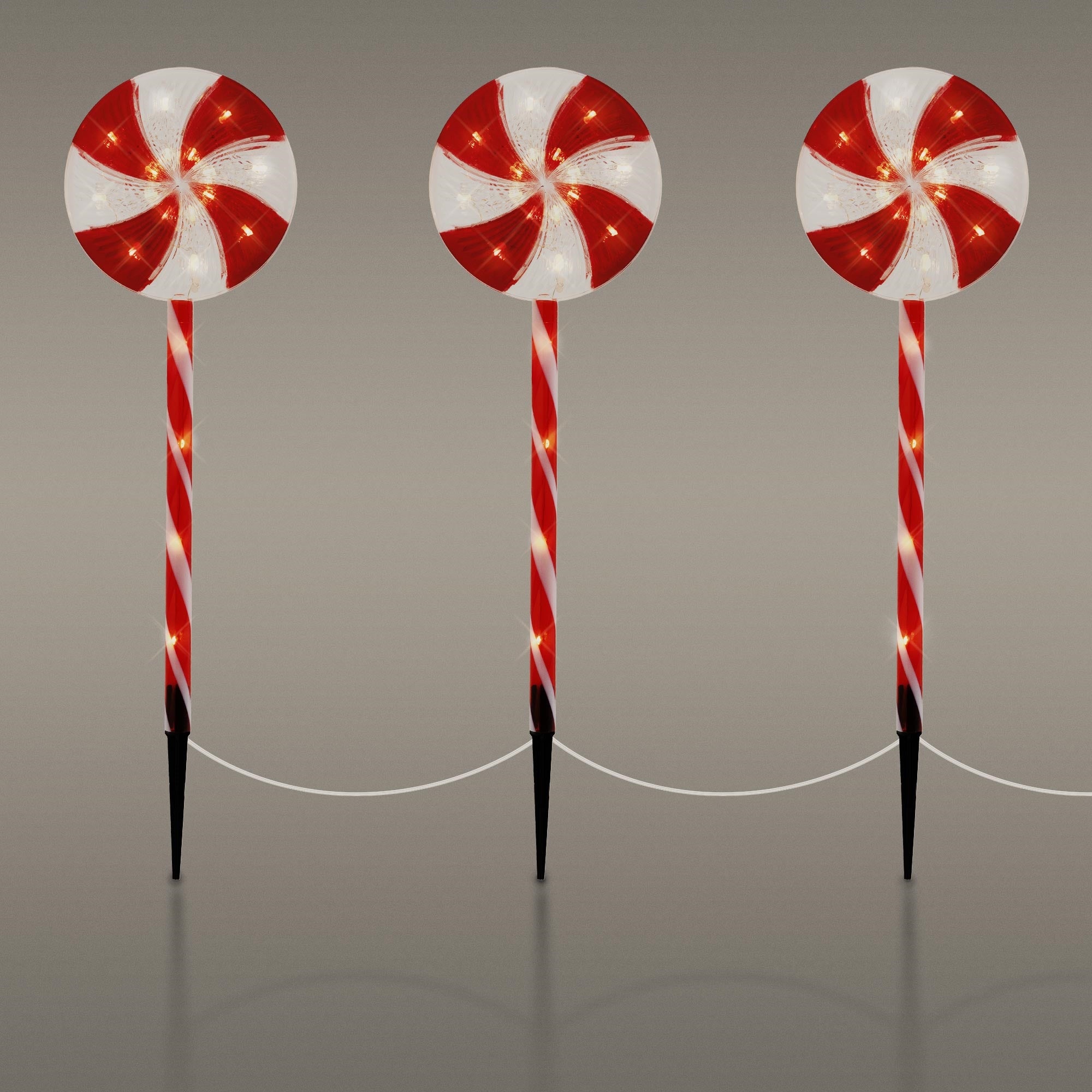 Tres grandes piruletas rojas y blancas en palos, dispuestas decorativamente.