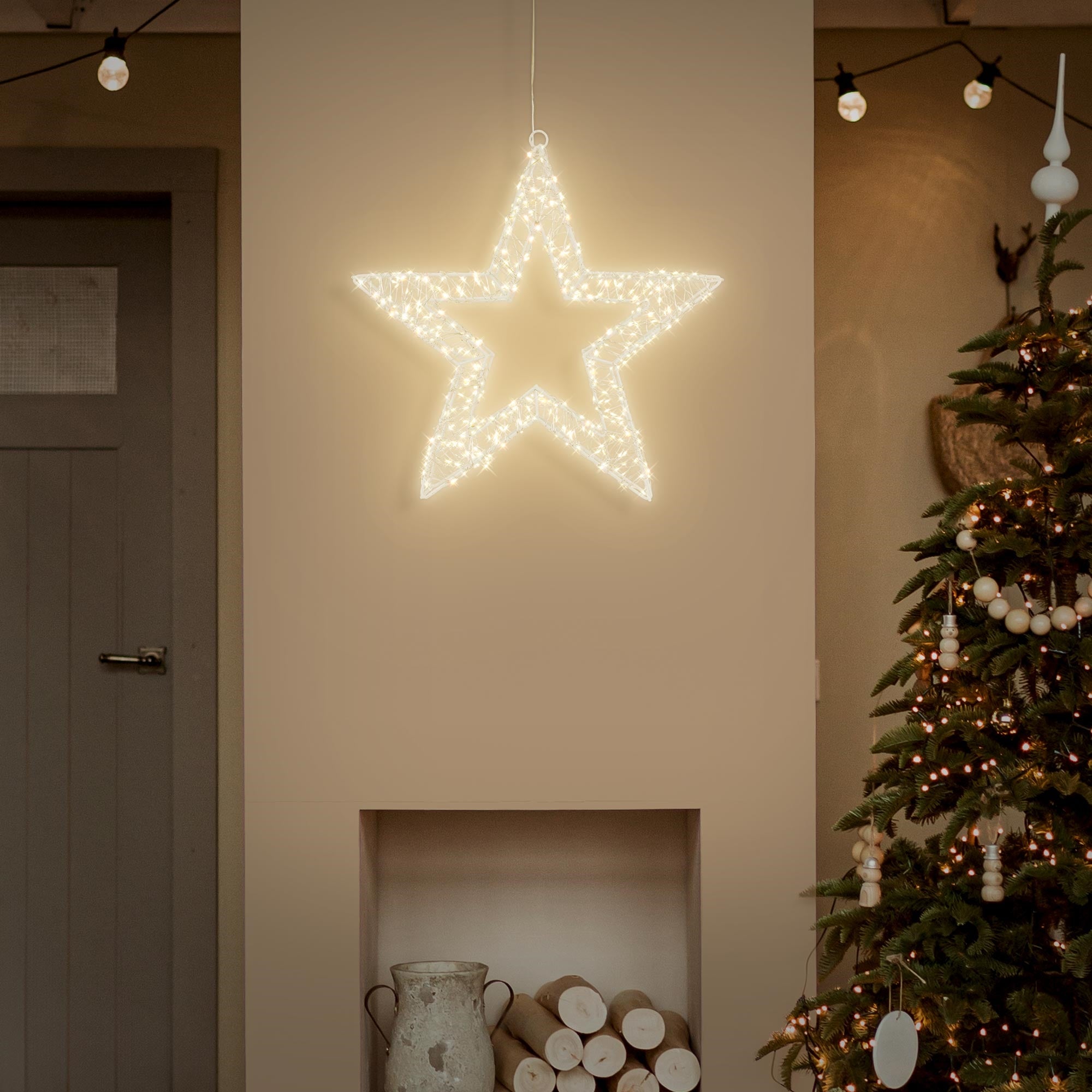 Leuchtender, weißer Stern hängt an einer Wand über einem Weihnachtsbaum.
