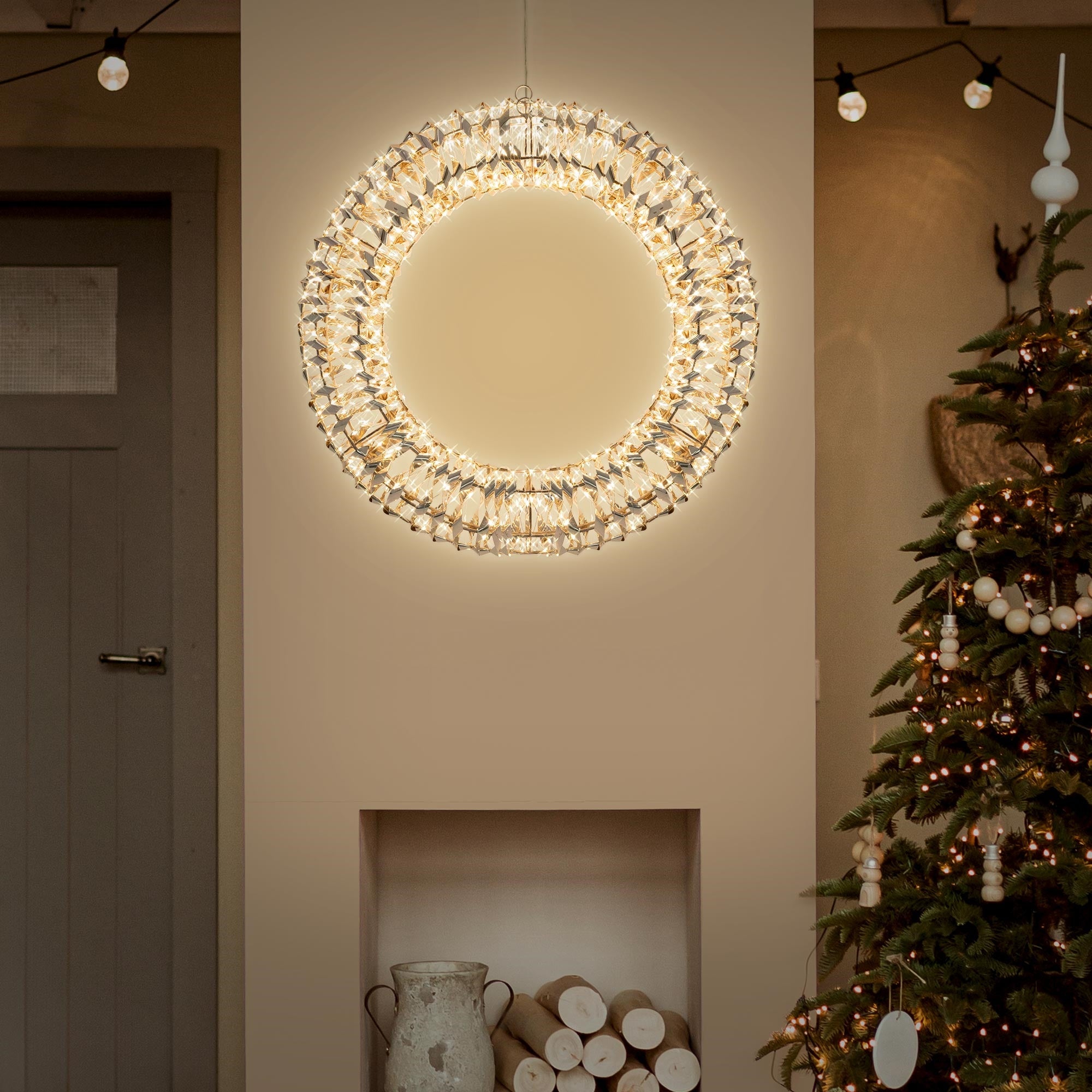 Lichtkranz hängt an Wand, neben einem Weihnachtsbaum und dekorativen Elementen.