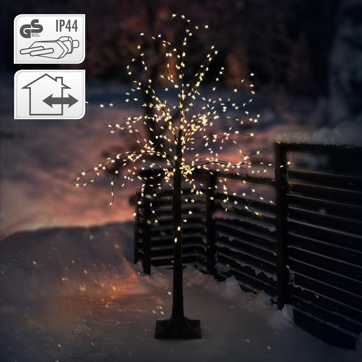 Beleuchteter Baum mit Lichtern im Schnee, umgeben von einem Zaun.