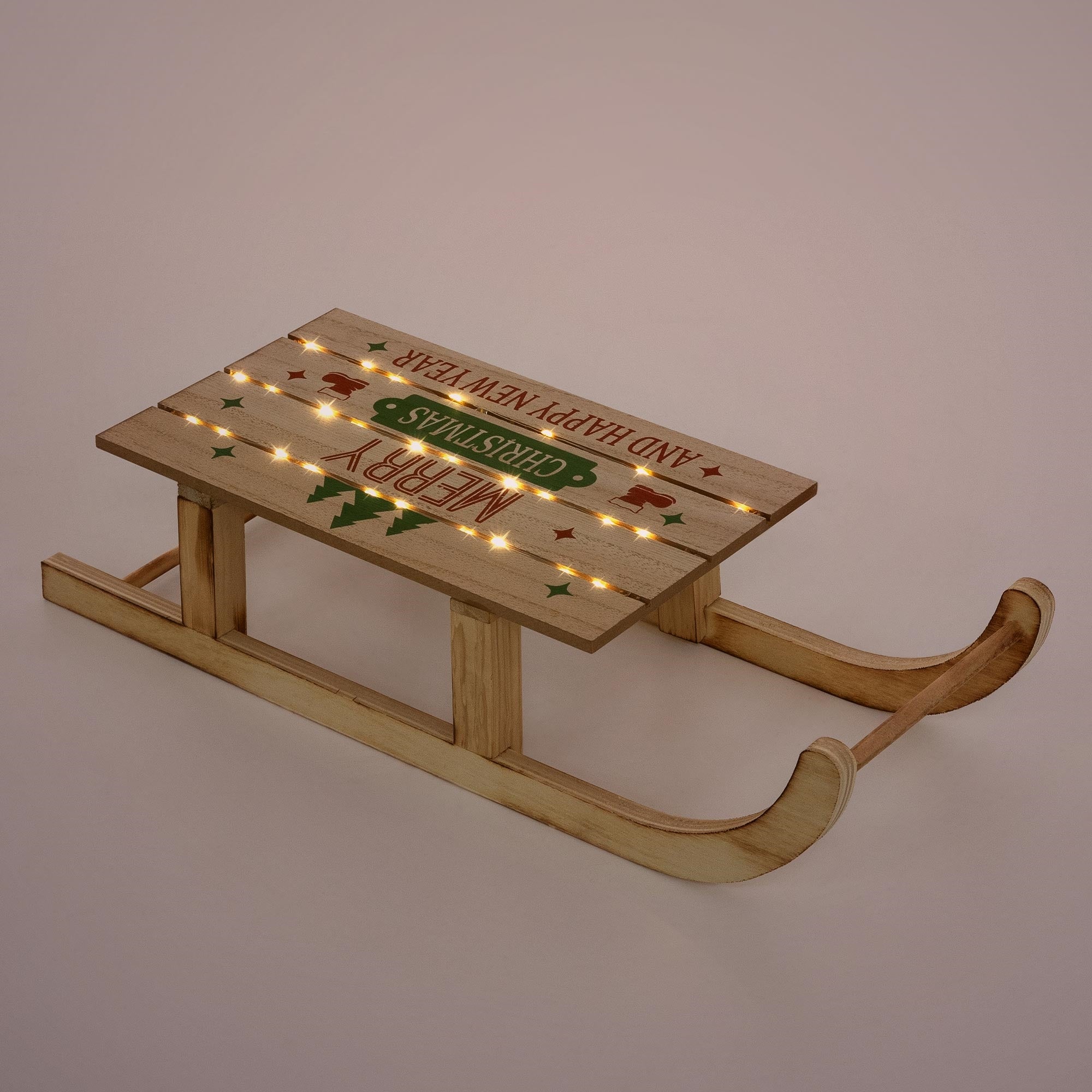 Slitta di legno con auguri natalizi e luci su uno sfondo uniforme.