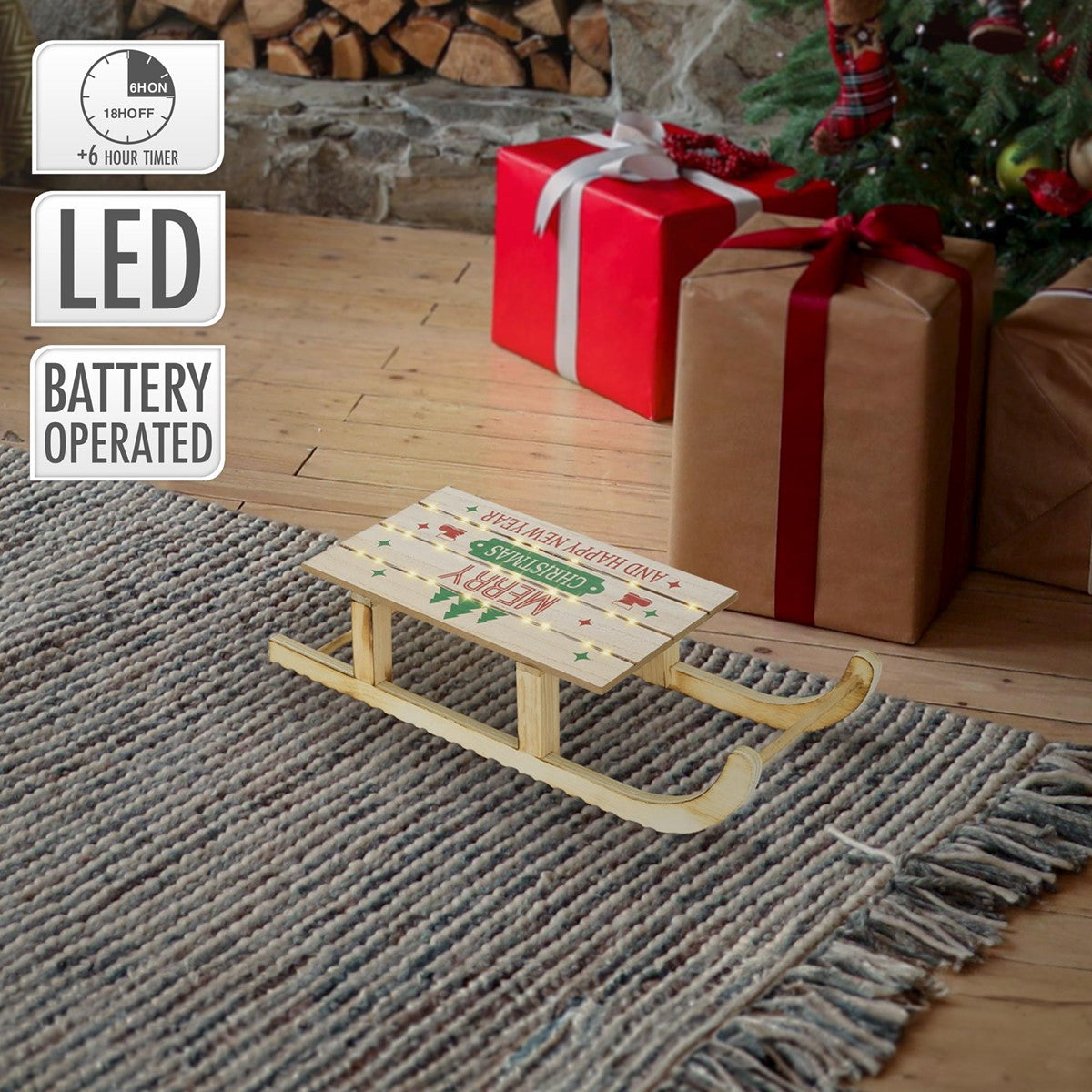 Ein kleiner Holzschlitten mit Weihnachtsmotiv vor einem Weihnachtsbaum und Geschenken.