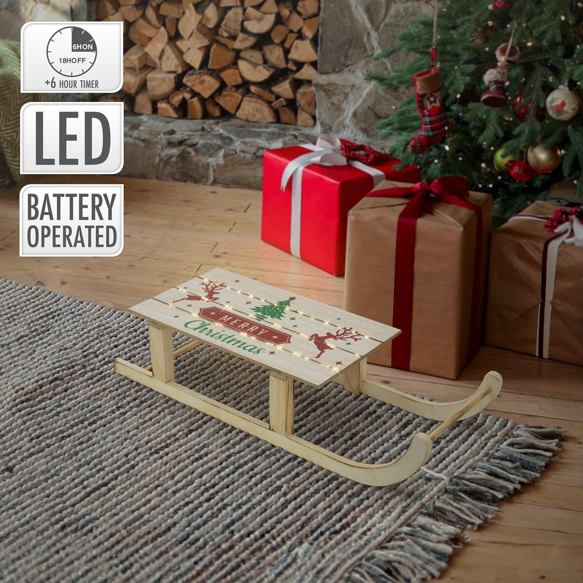 Ein kleiner Holzschlitten mit Weihnachtsmotiv vor einem Weihnachtsbaum und Geschenken.