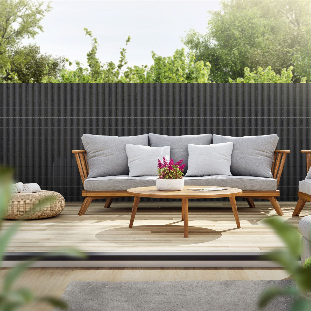 Gemütliche Terrasse mit Sofa, Tisch und Pflanzen im Hintergrund.