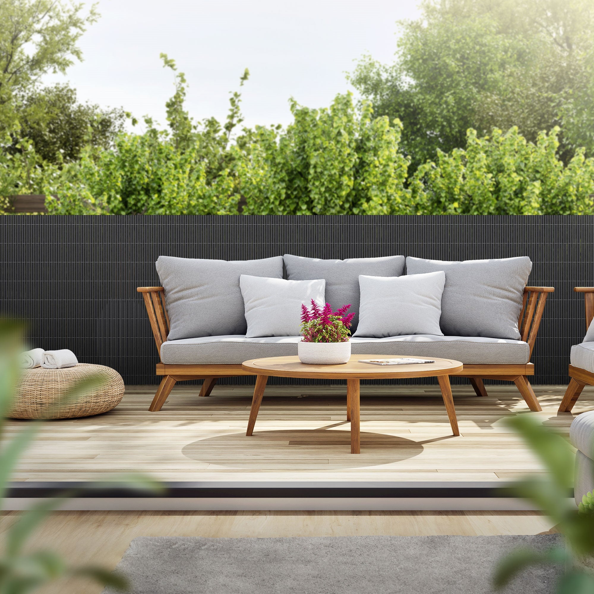 Gemütliche Sitzecke mit grauem Sofa, runden Tisch und Pflanzen im Hintergrund.