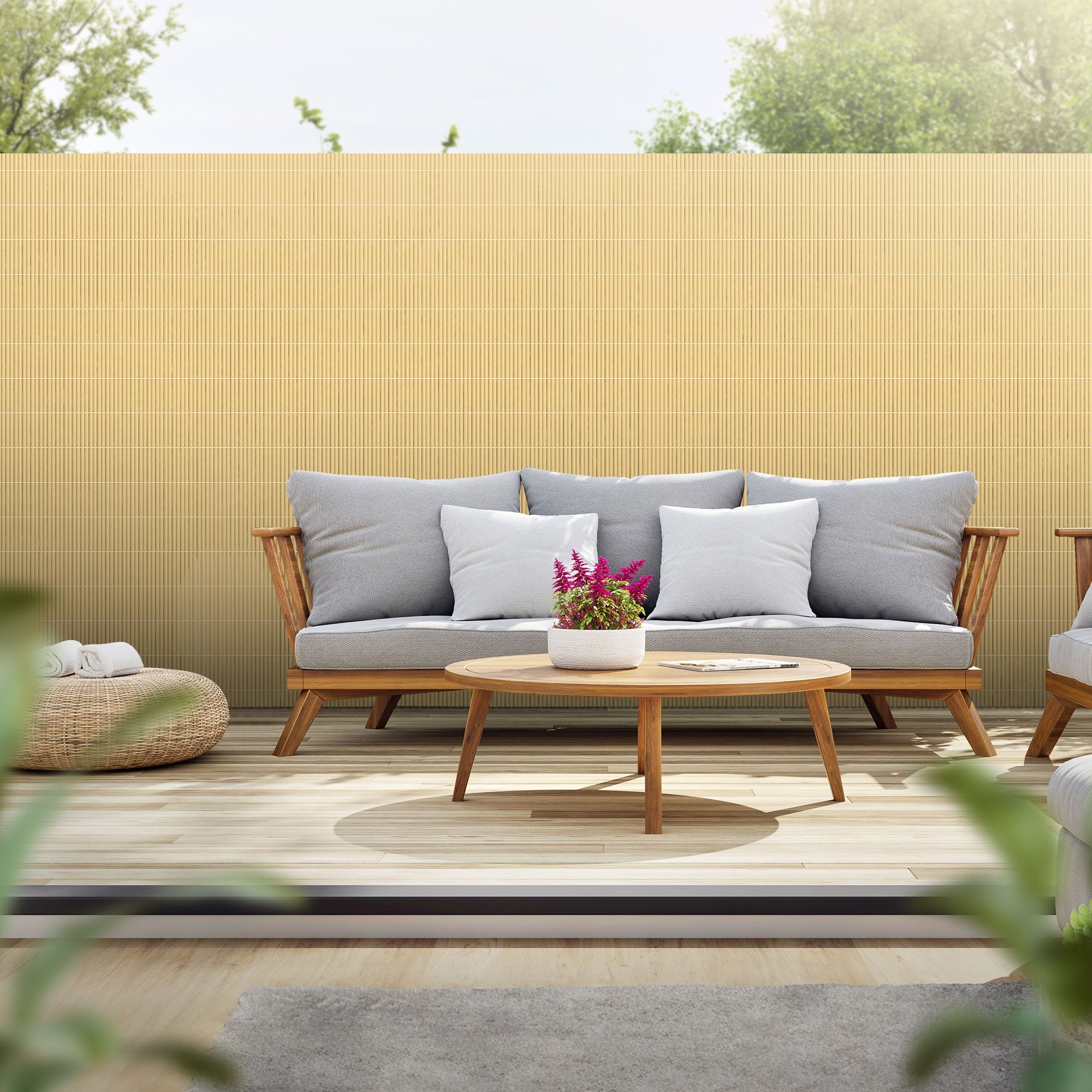 Sofa med puder og bord på en terrasse, omgivet af planter og en lys baggrund.