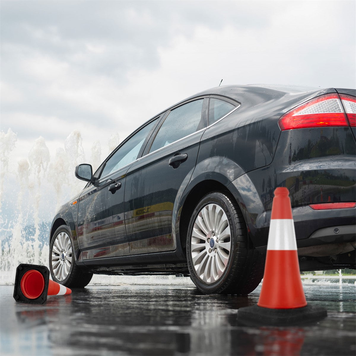 Schwarzes Auto neben roten Verkehrshütchen auf nasser Straße.