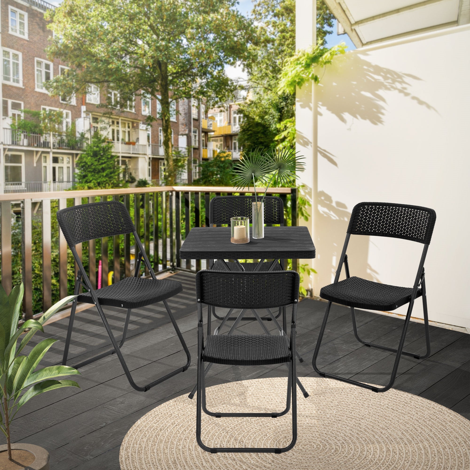Terrasse med fire sorte klapstole og et bord, omgivet af planter.
