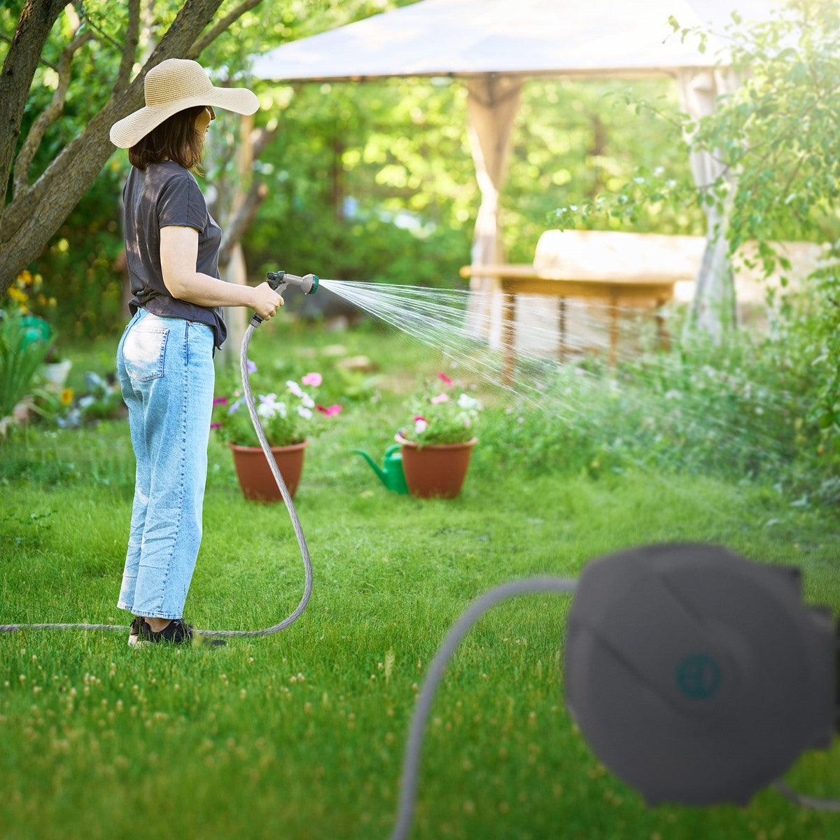 Femme dans le jardin avec un tuyau, arrosant des plantes.