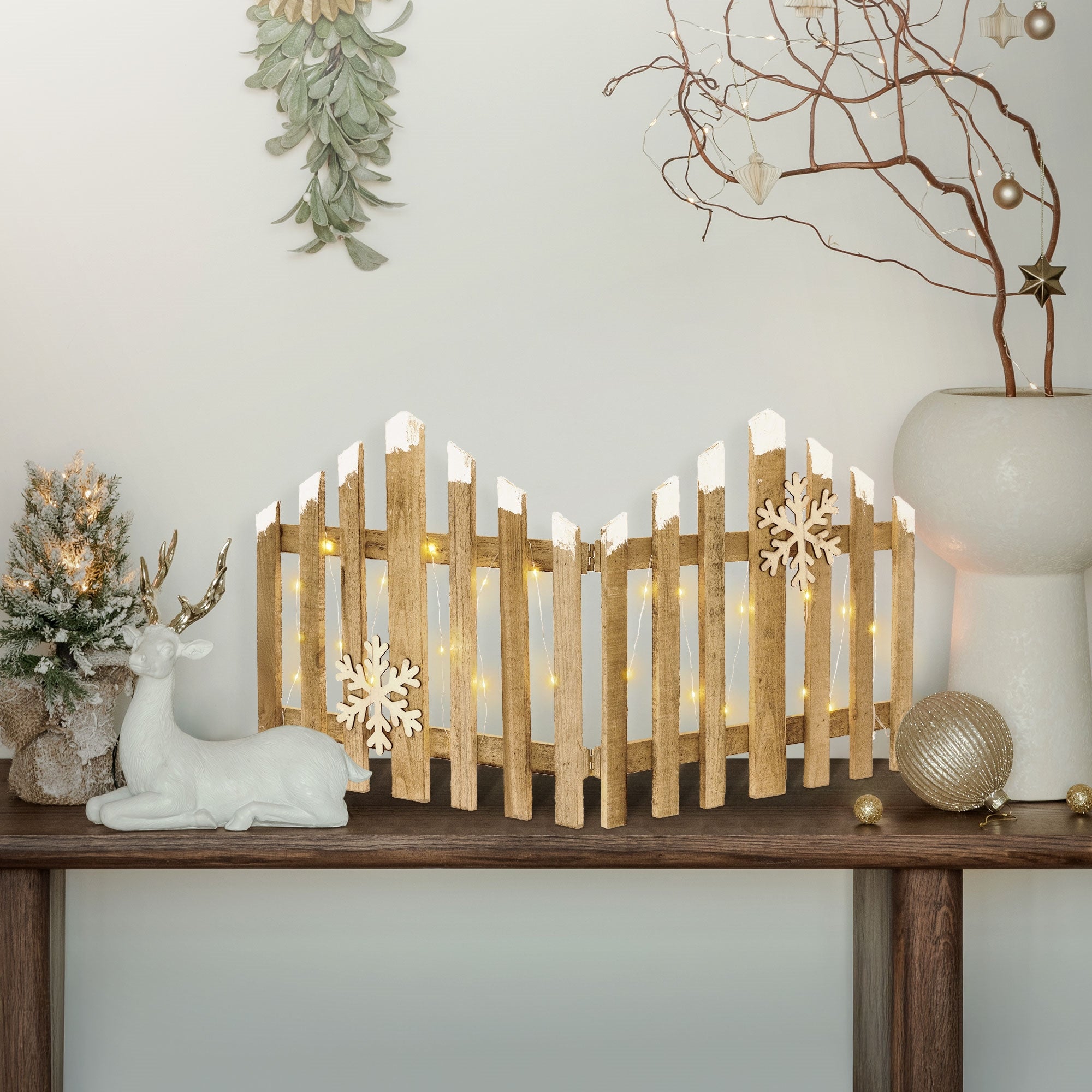 Dekorierter Tisch mit Holzzaun, Rehfigur und Weihnachtsbaum.