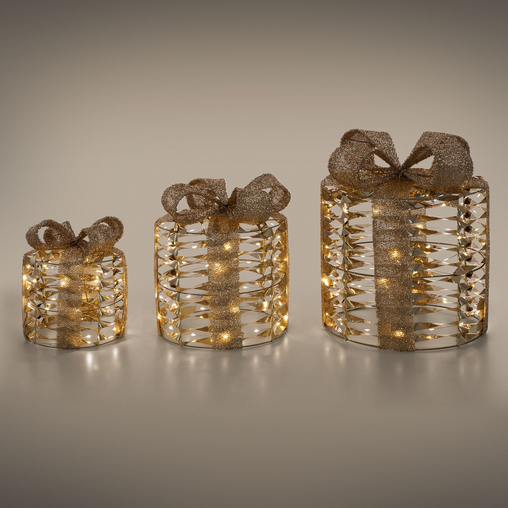 Drei Geschenke mit goldenen Schleifen und Lichtern auf einem grauen Hintergrund.