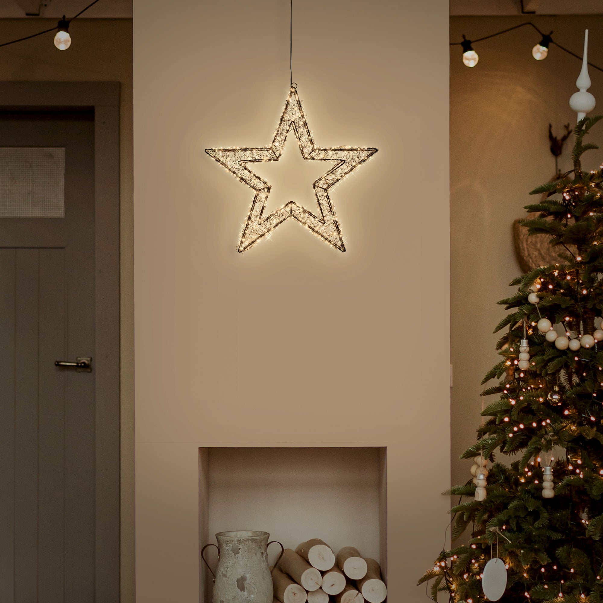 Ein beleuchteter Stern hängt an einer Wand über einem Weihnachtsbaum.