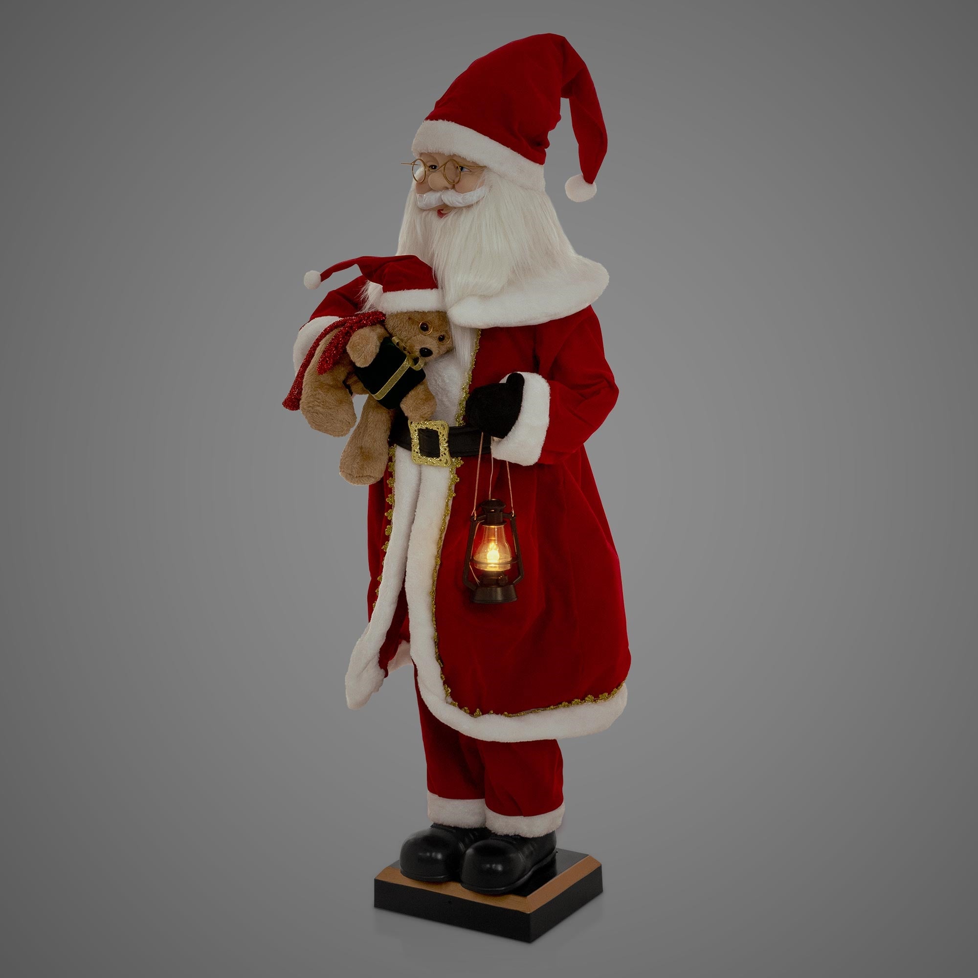 Eine Weihnachtsmannfigur mit einem Teddybär und einer Laterne in rotem Gewand.