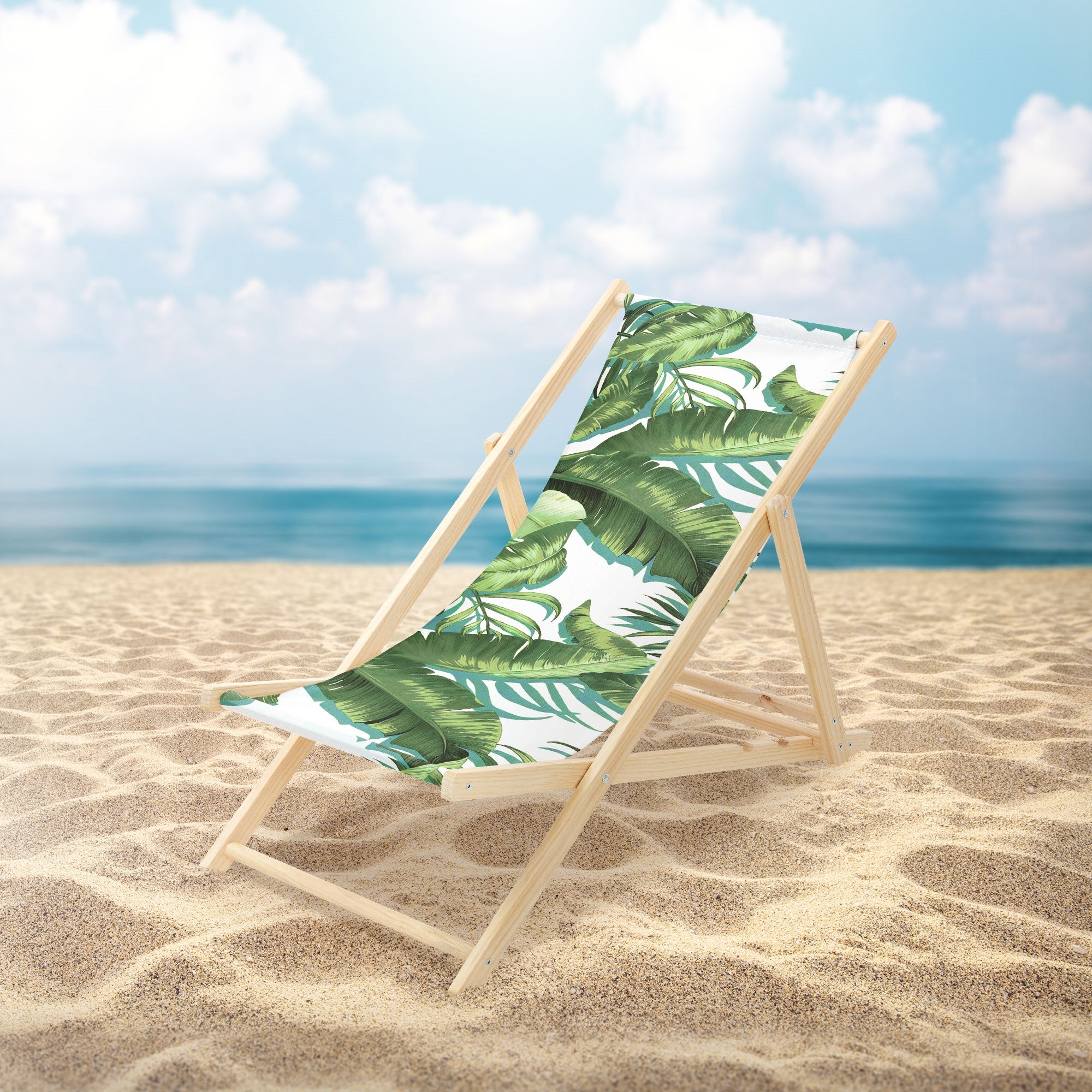 Liegestuhl mit grünem Blattmuster auf einem Sandstrand vor dem Meer.