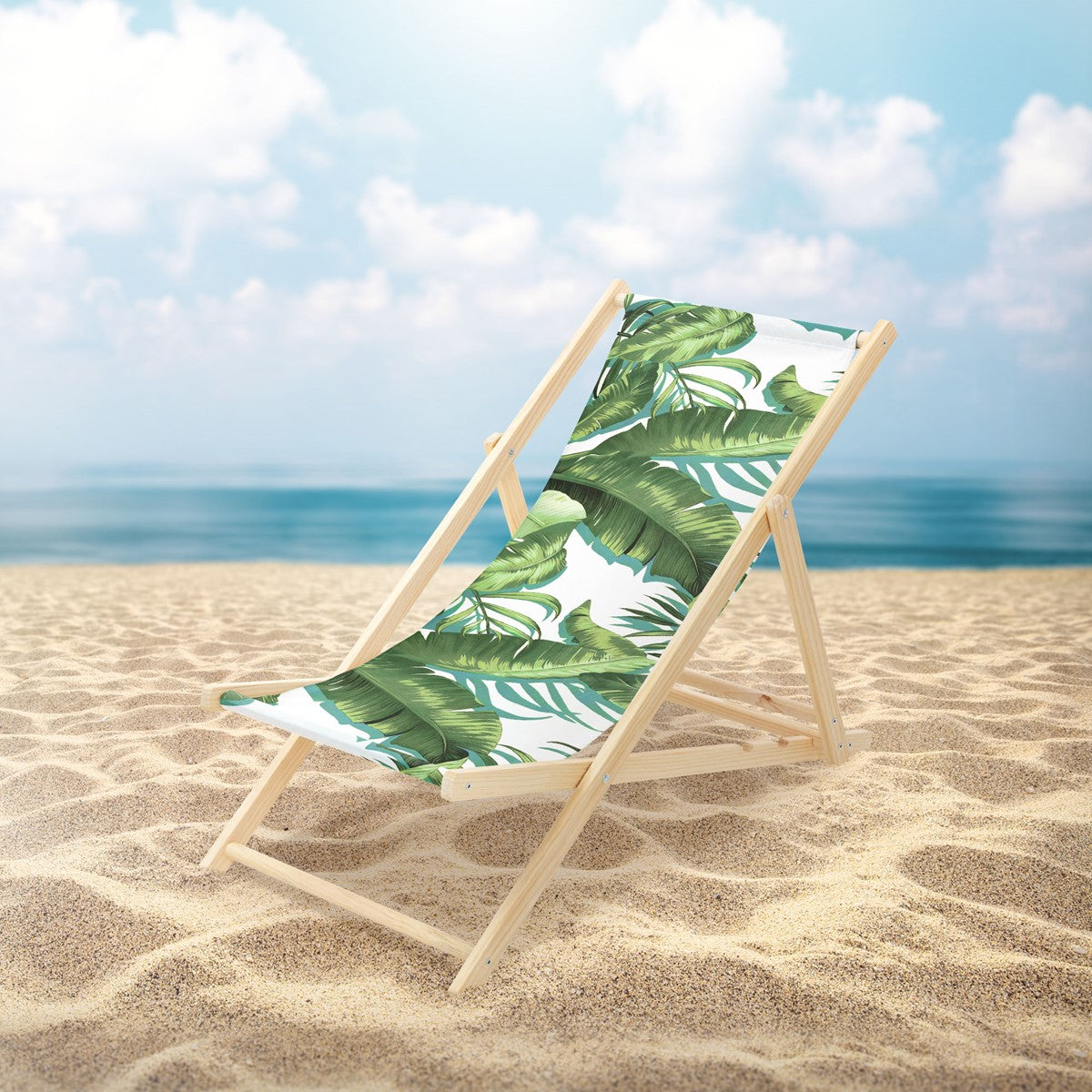 Liegestuhl mit grünem Blattmuster auf einem Sandstrand vor dem Meer.
