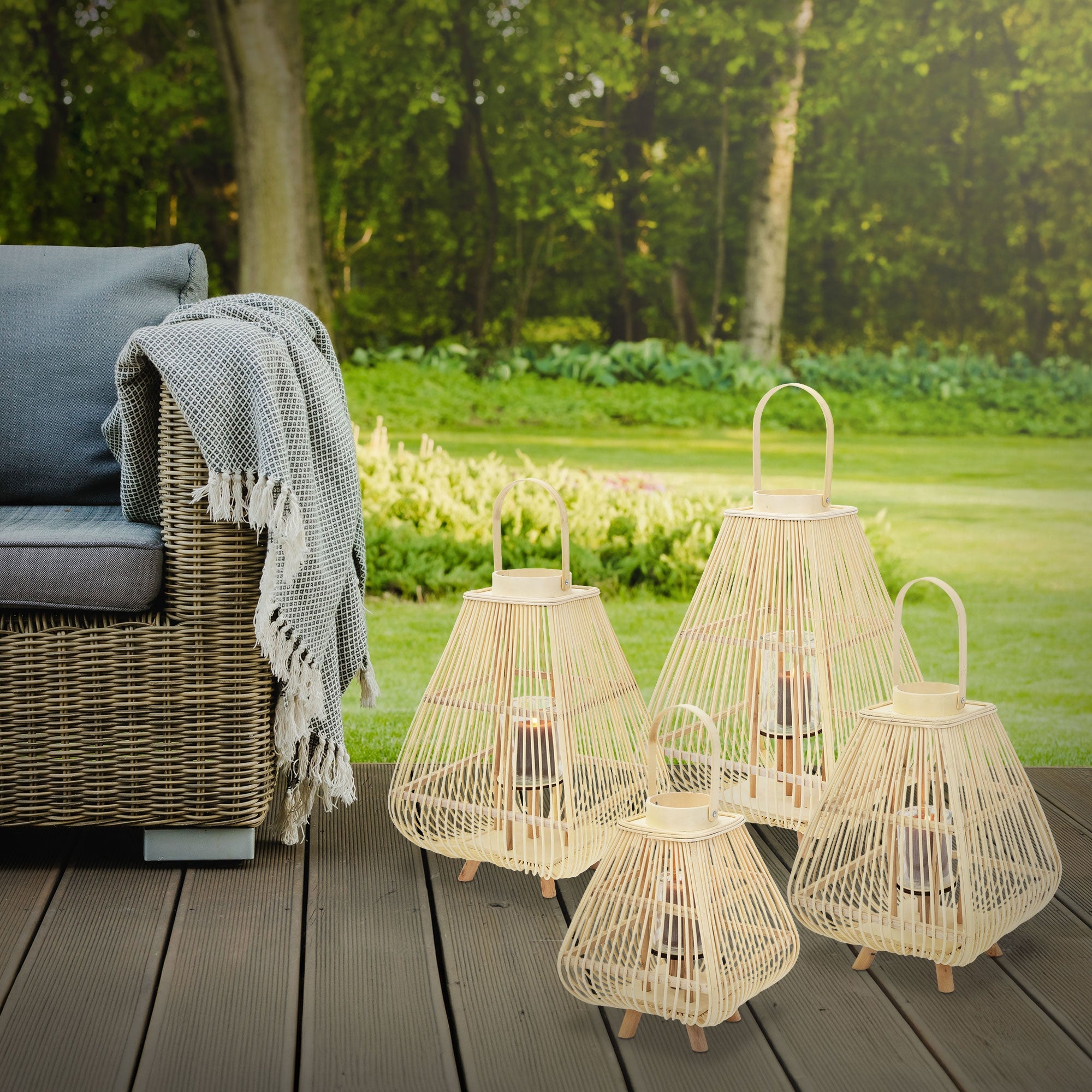 Four lanterns are standing on a wooden deck next to a sofa and a blanket.