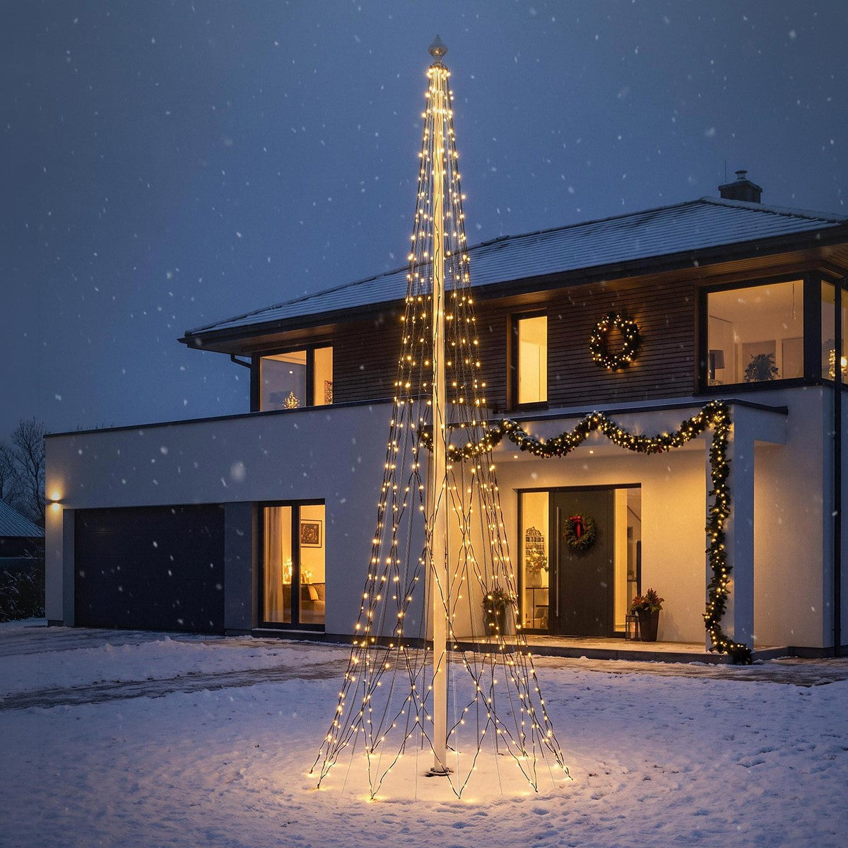 Beleuchteter Weihnachtsbaum vor einem modernen Haus im Schnee.
