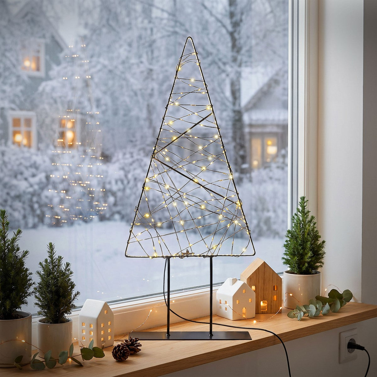 Leuchtender Weihnachtsbaum aus Draht vor einem Fenster mit Schnee.