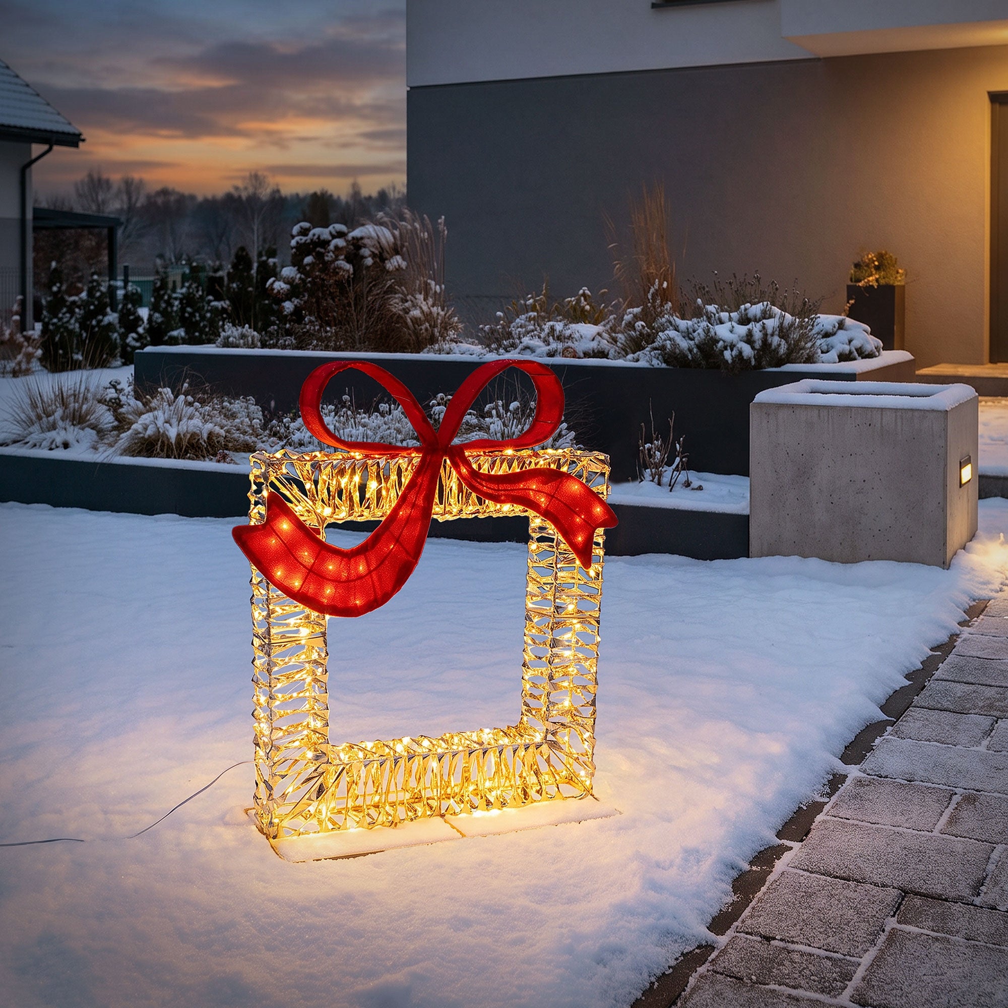 Beleuchteter LED-Rahmen mit rotem Schleifenmotiv im Schnee.
