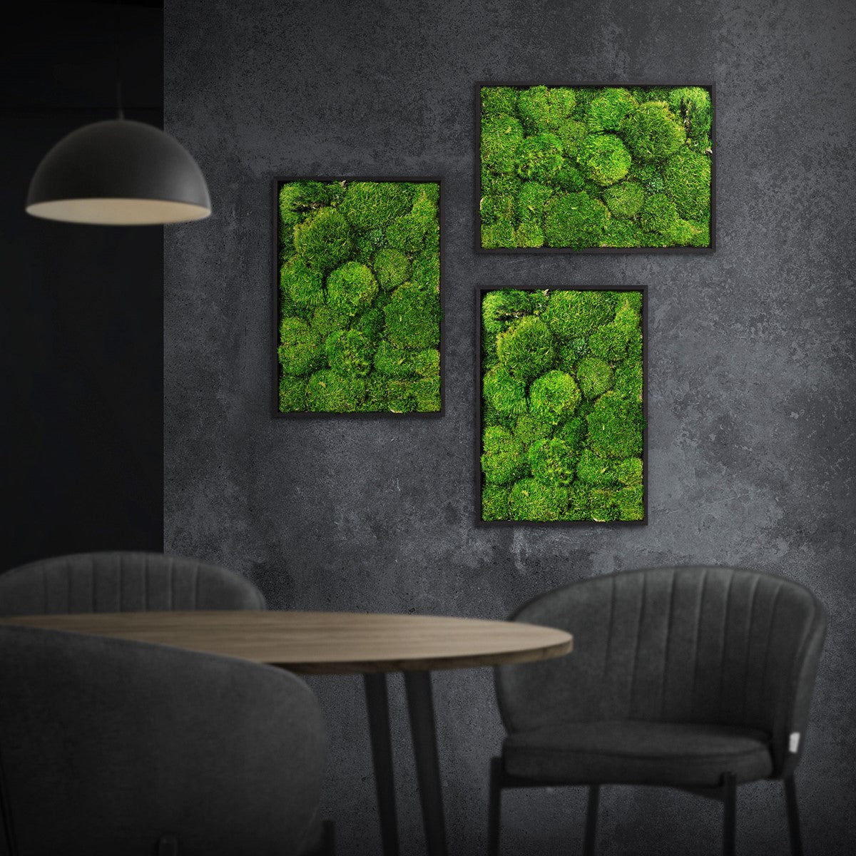 Drei gerahmte Moosbilder hängen an einer dunklen Wand über einem Tisch mit zwei Stühlen.