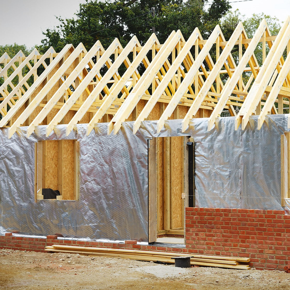 Haus im Rohbau mit silberner Dämmfolie, roten Ziegeln und offenem Dachstuhl aus hellem Holz.