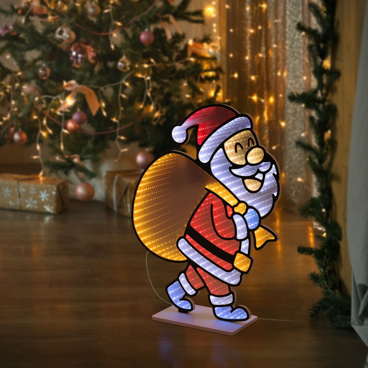 Leuchtende Weihnachtsmannfigur mit Sack, vor einem Weihnachtsbaum.