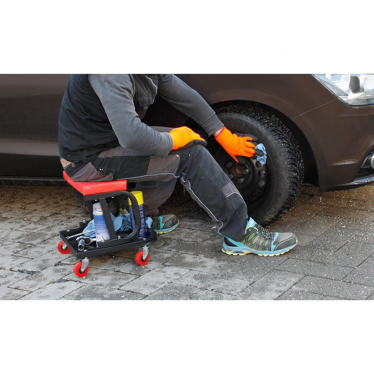 Persoon in handschoenen reinigt een autoband, zittend op een werkplaatsstoel.