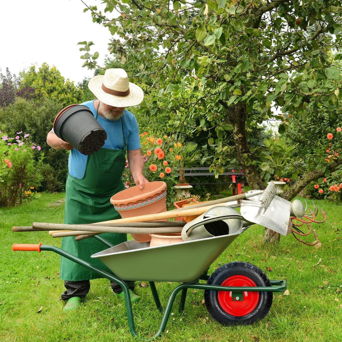 Man met hoed die potten in een kruiwagen in de tuin houdt.