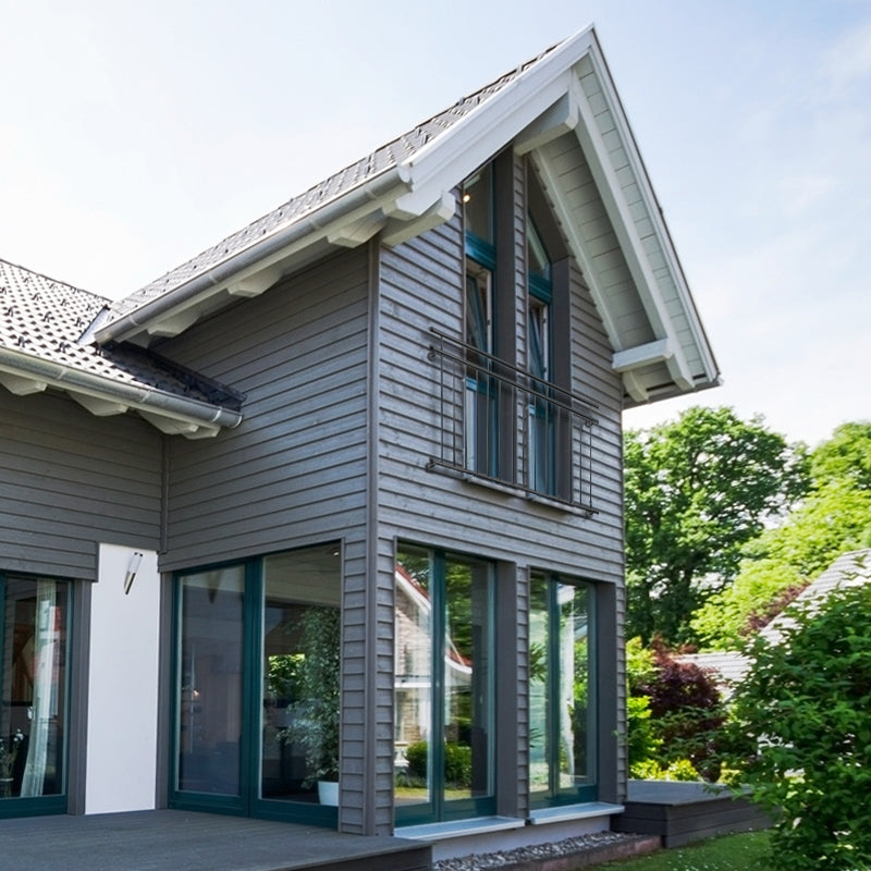Hus med skråtag, store vinduer og træbeklædning.