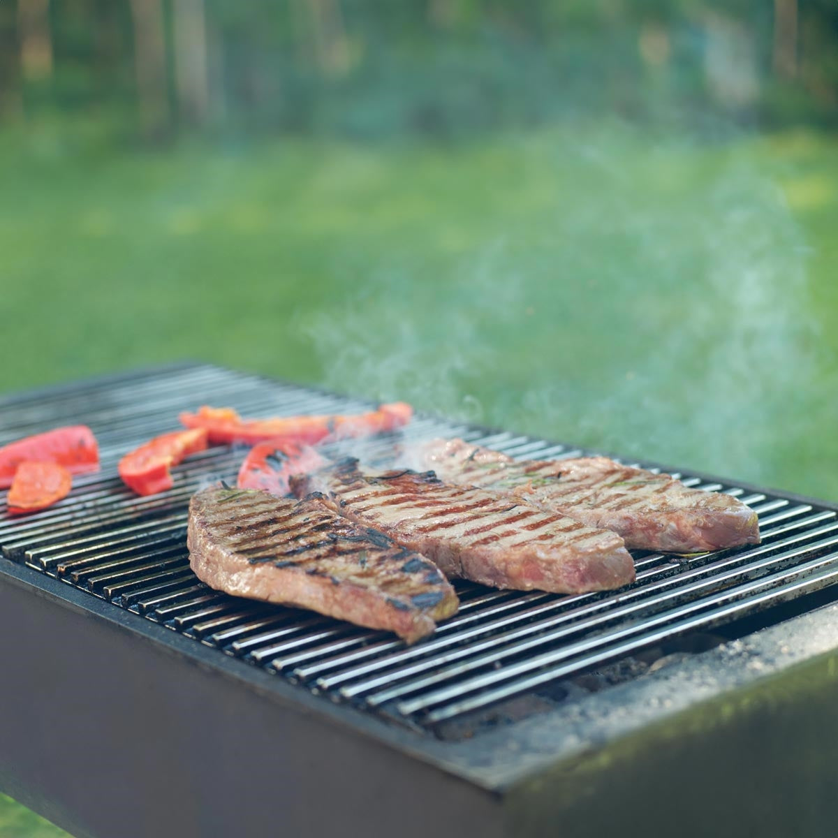Drei gegrillte Steaks auf einem Grill mit rauchendem Hintergrund.