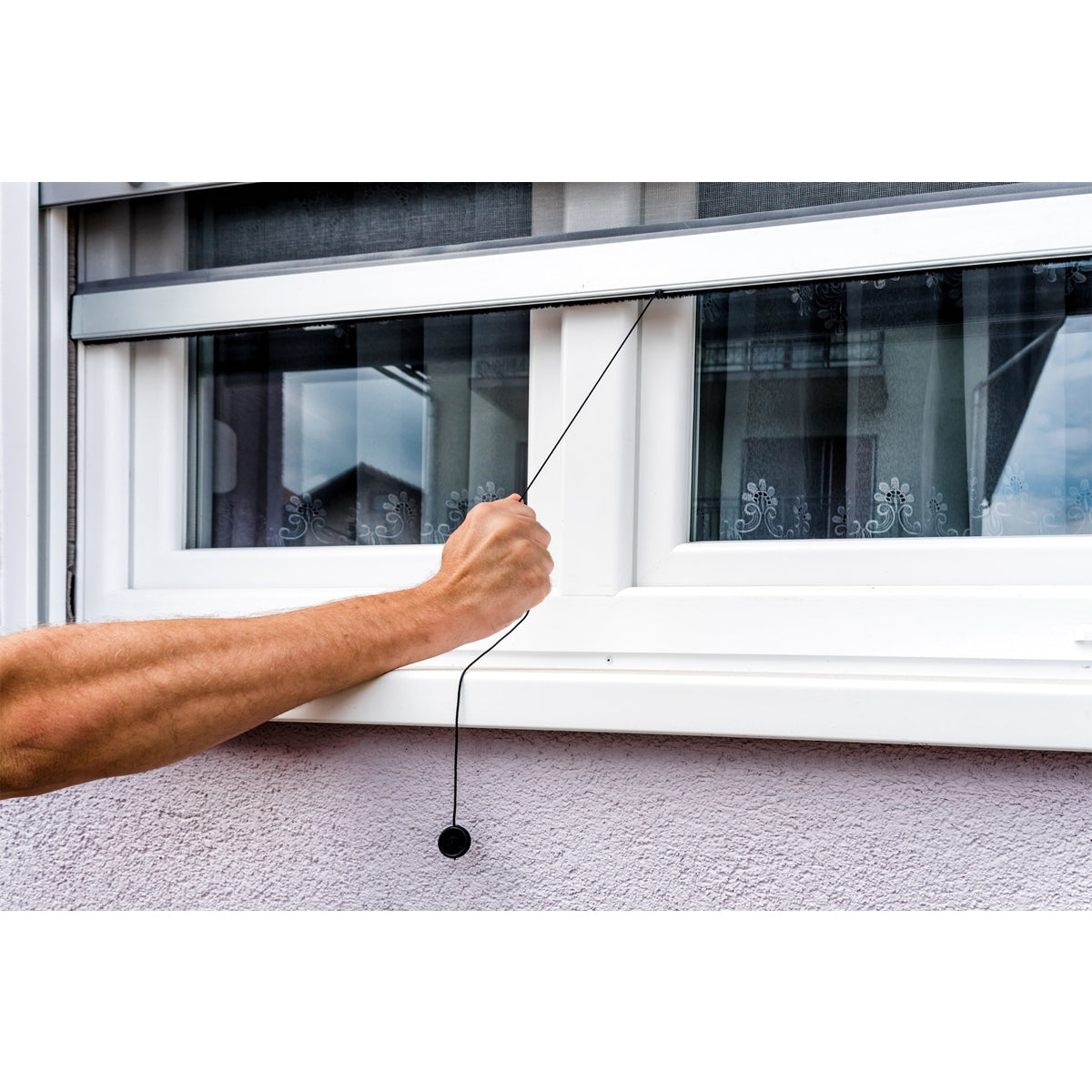 Hand zieht an der Schnur eines Insektenschutzgitters am Fenster.