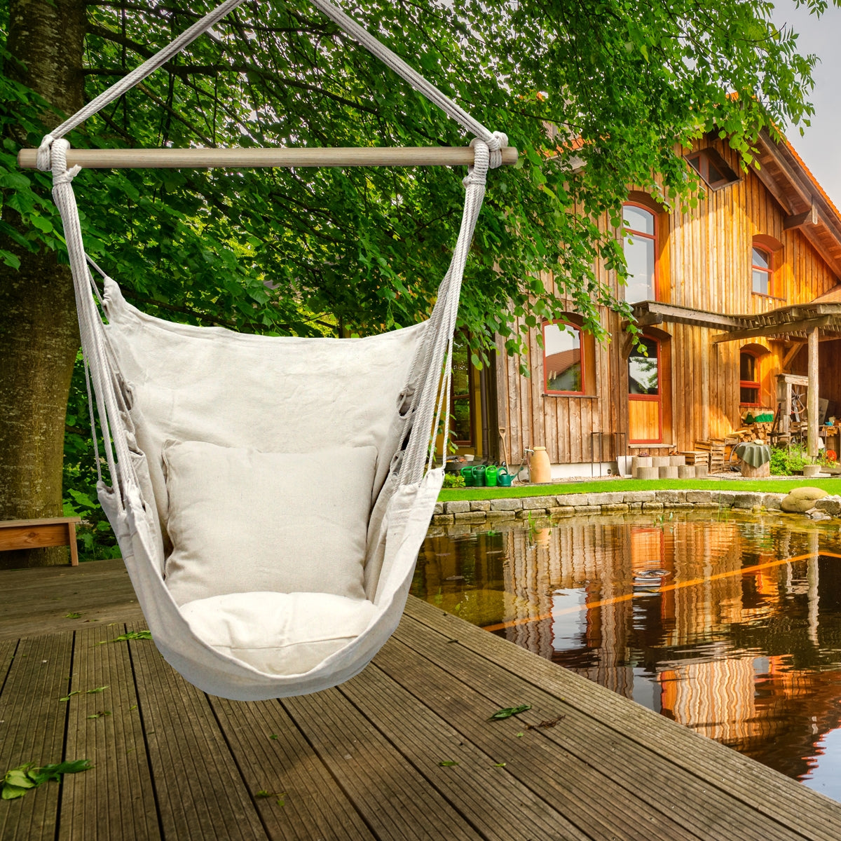 Hängesessel aus hellem Stoff, vor einem Holzhaus am Wasser.