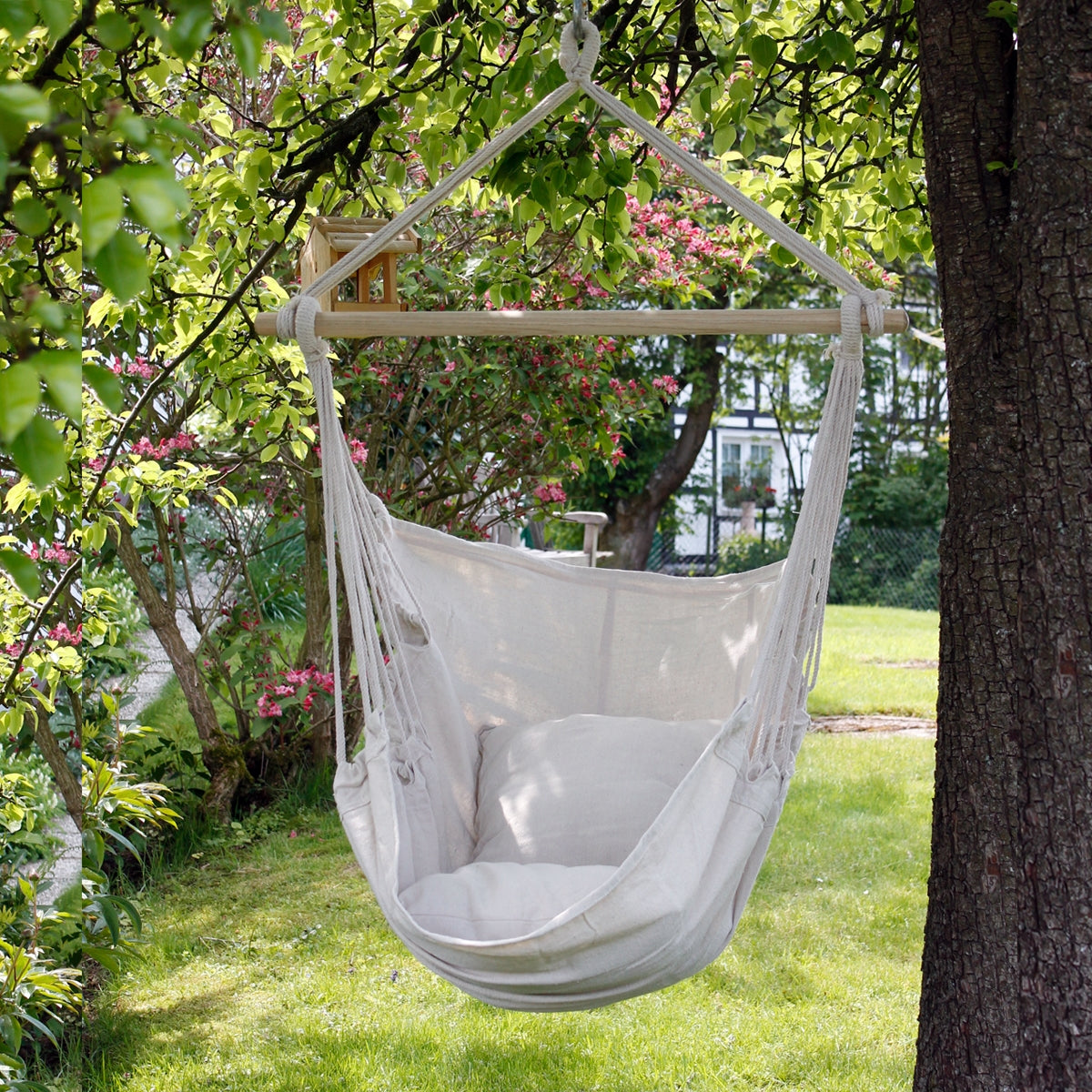 Hängesessel aus hellem Stoff, aufgehängt in einem Garten mit blühenden Bäumen.