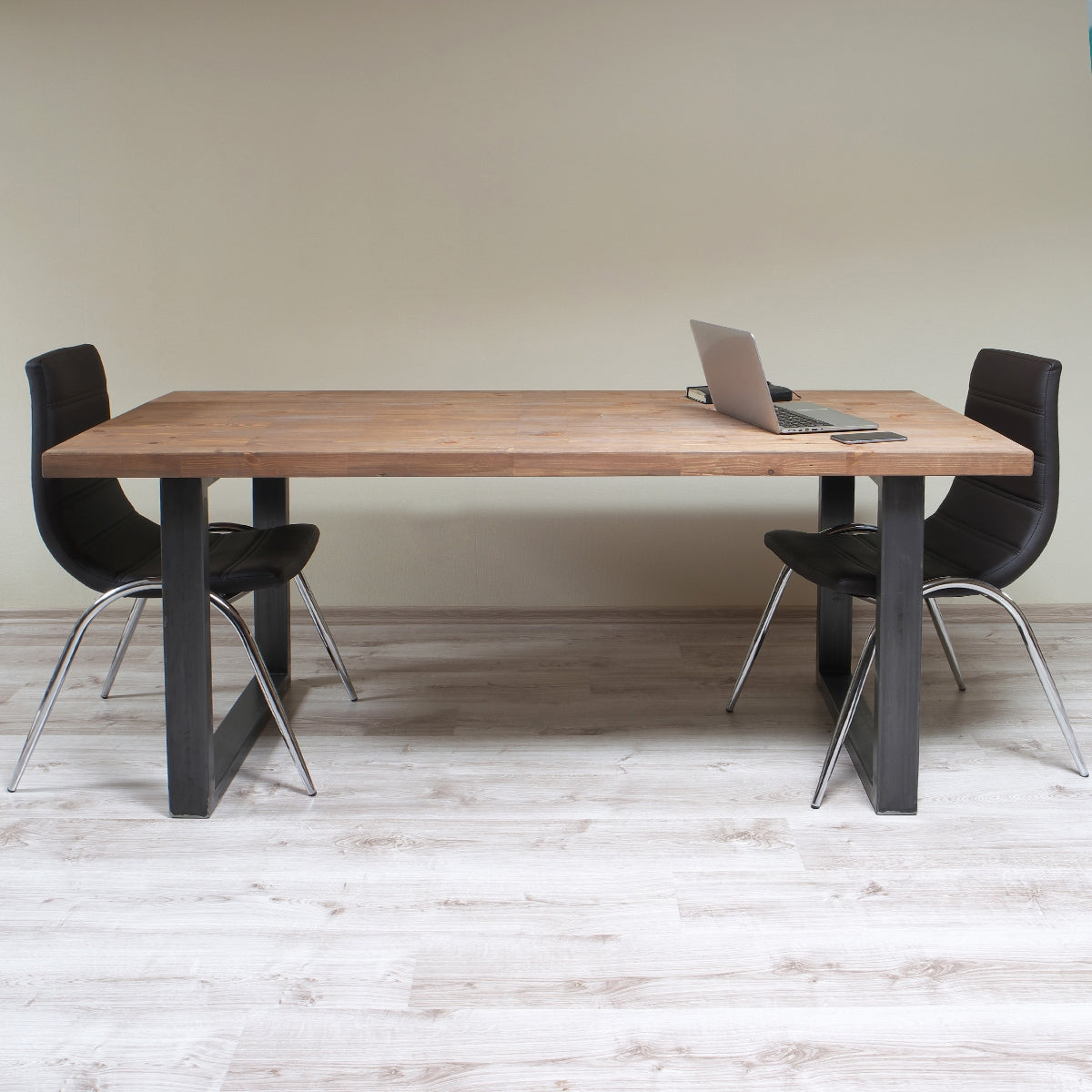 Wooden table with laptop and two black chairs, on light floor.