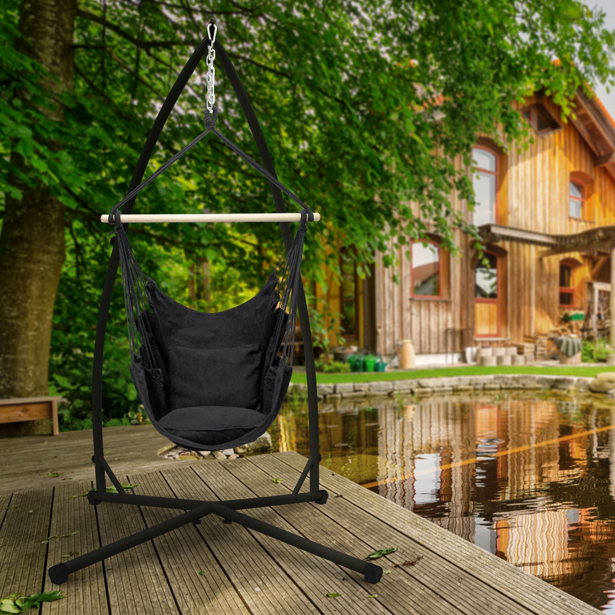 Hängesessel in schwarzer Farbe, auf Holzdeck mit Blick auf ein Haus und Teich.