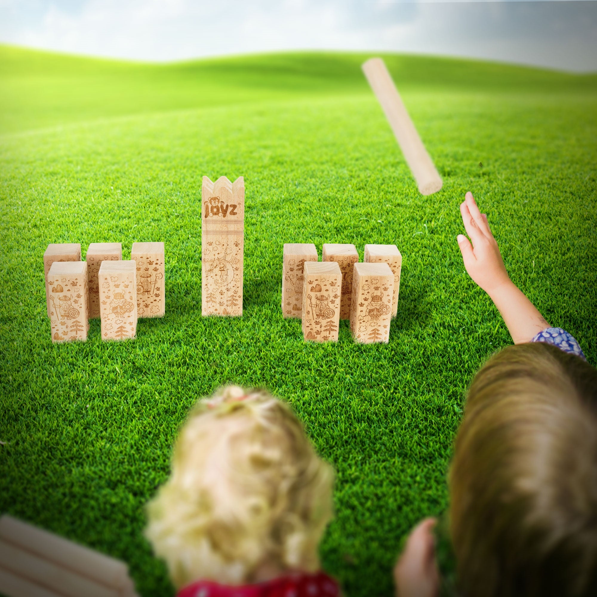 Zwei Kinder spielen mit Holzbausteinen auf einer Wiese.