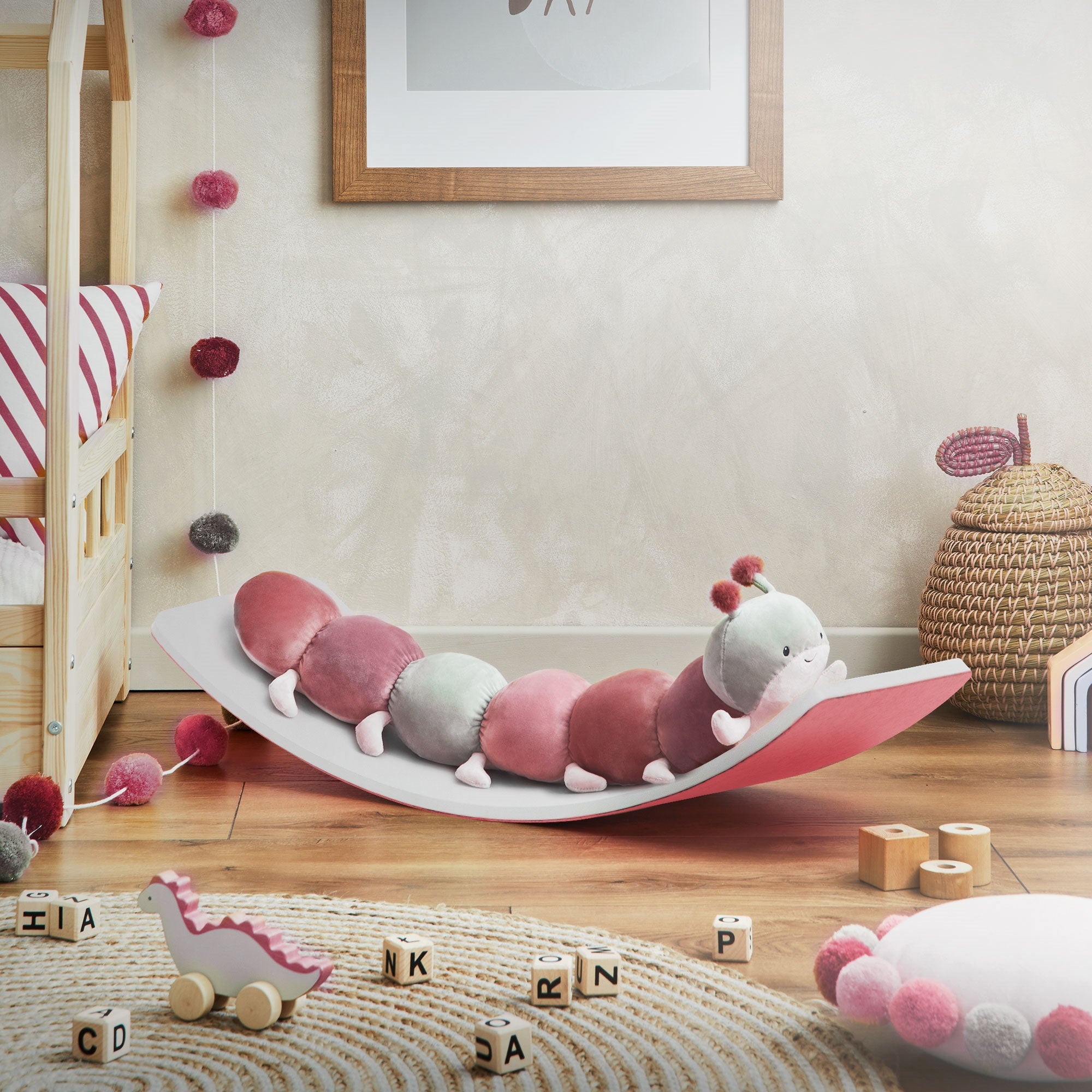Ein Wackelbrett mit einem rosa und grünen Raupen-Spielzeug. Spielzeug und Dekoration im Hintergrund.