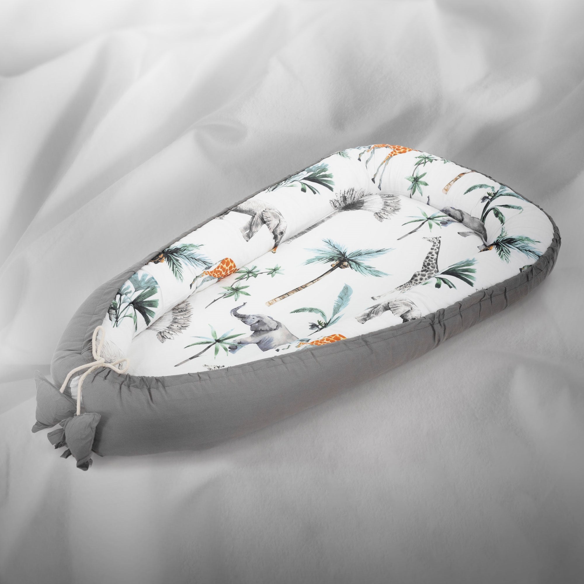 Un nid pour bébé avec des motifs d'animaux et des palmiers sur fond gris.
