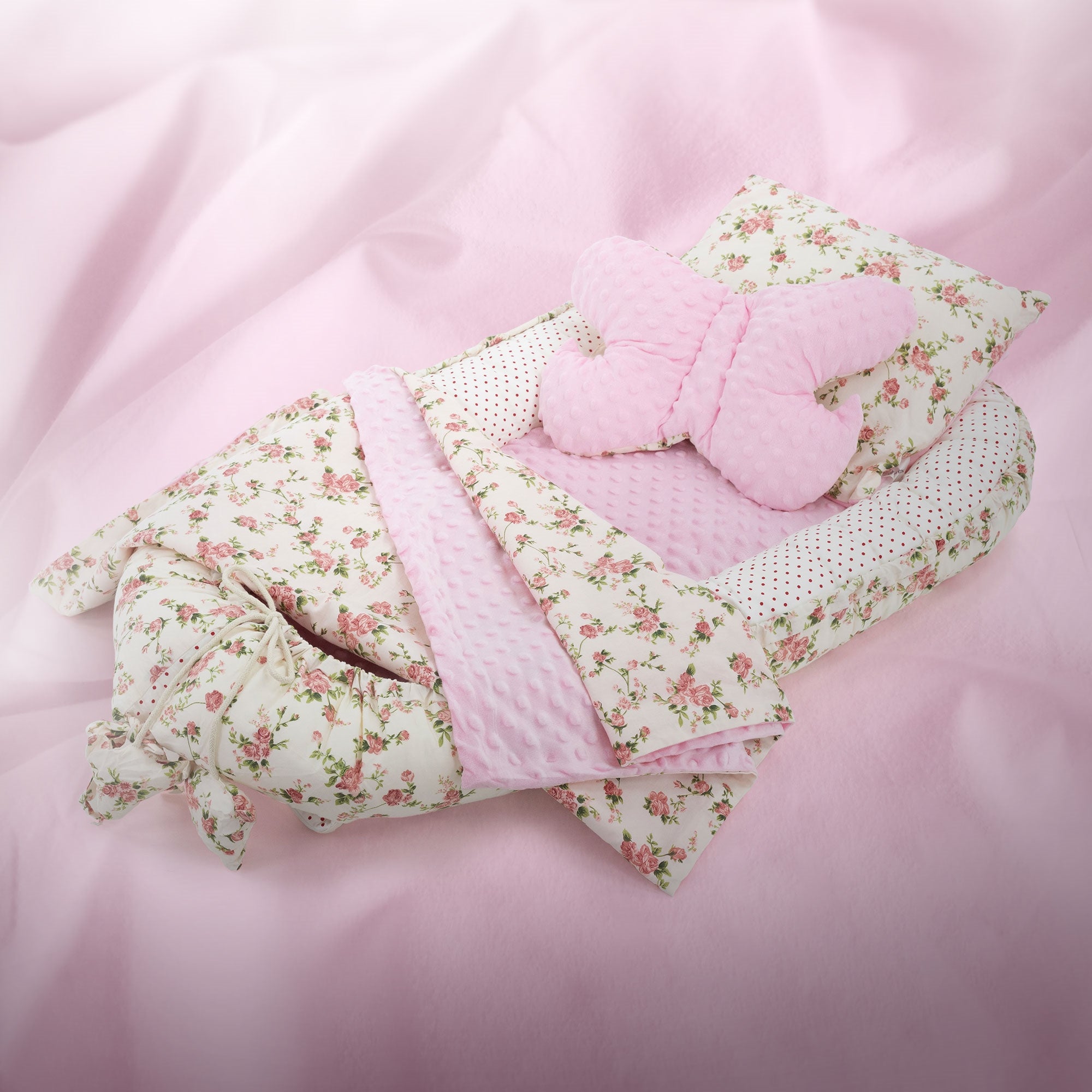 Ein Babybettchen mit rosa Decke und Kissen mit Blumenmuster.
