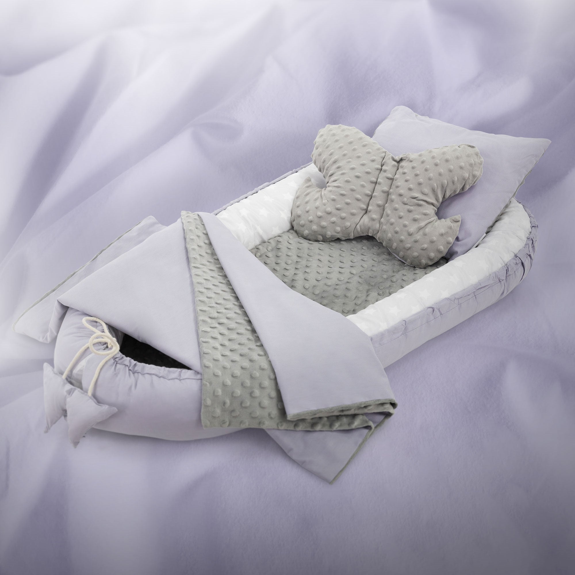 Een grijs babybed met een vlinderkussen en een deken.