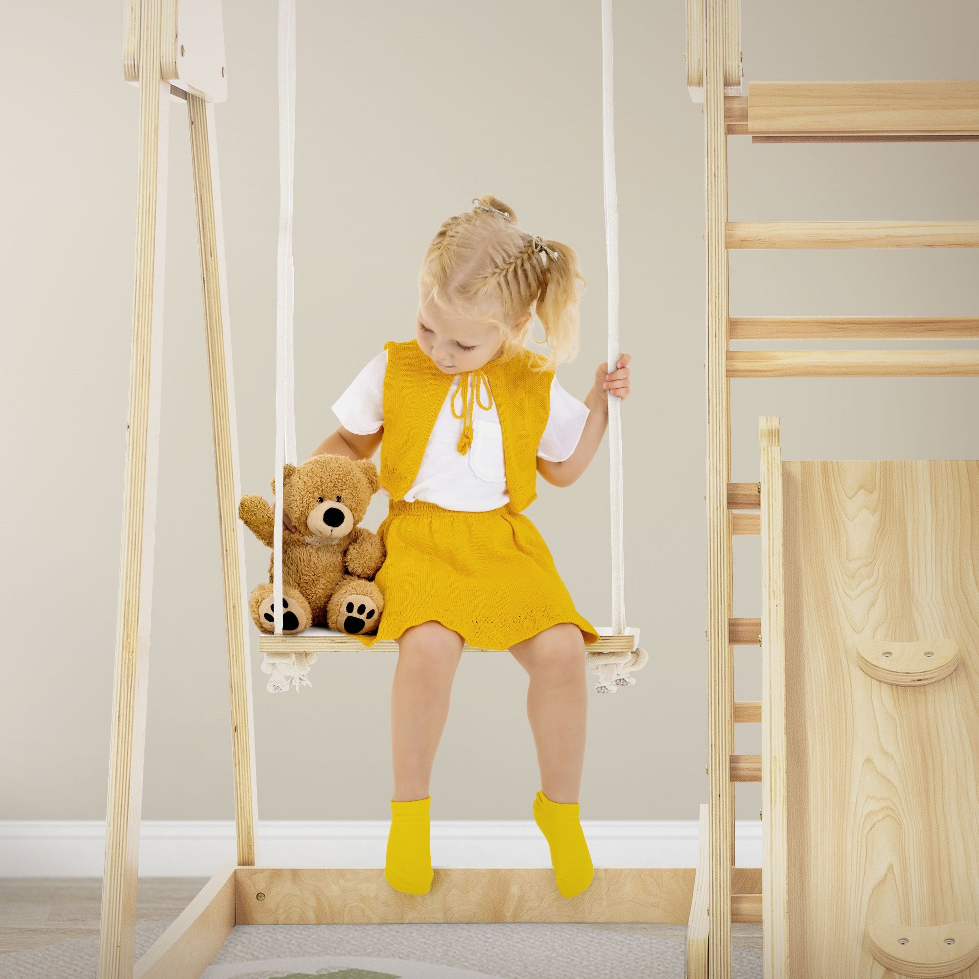 Un niño con un vestido amarillo se balancea y sostiene un oso de peluche.