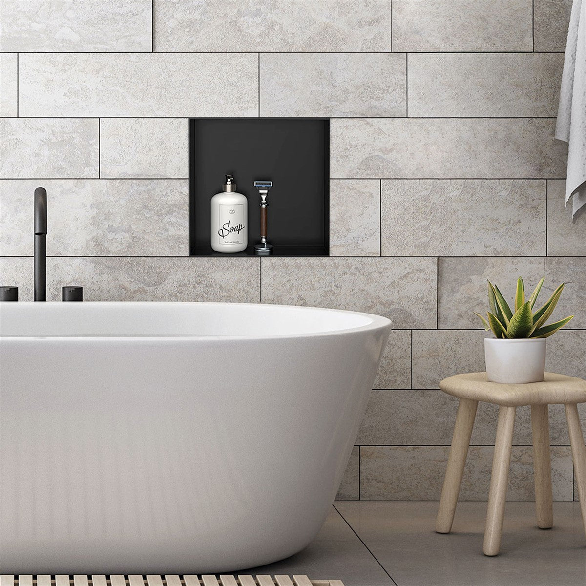 Freistehende Badewanne vor einer grauen Wand mit Nische für Seife und Rasierer.