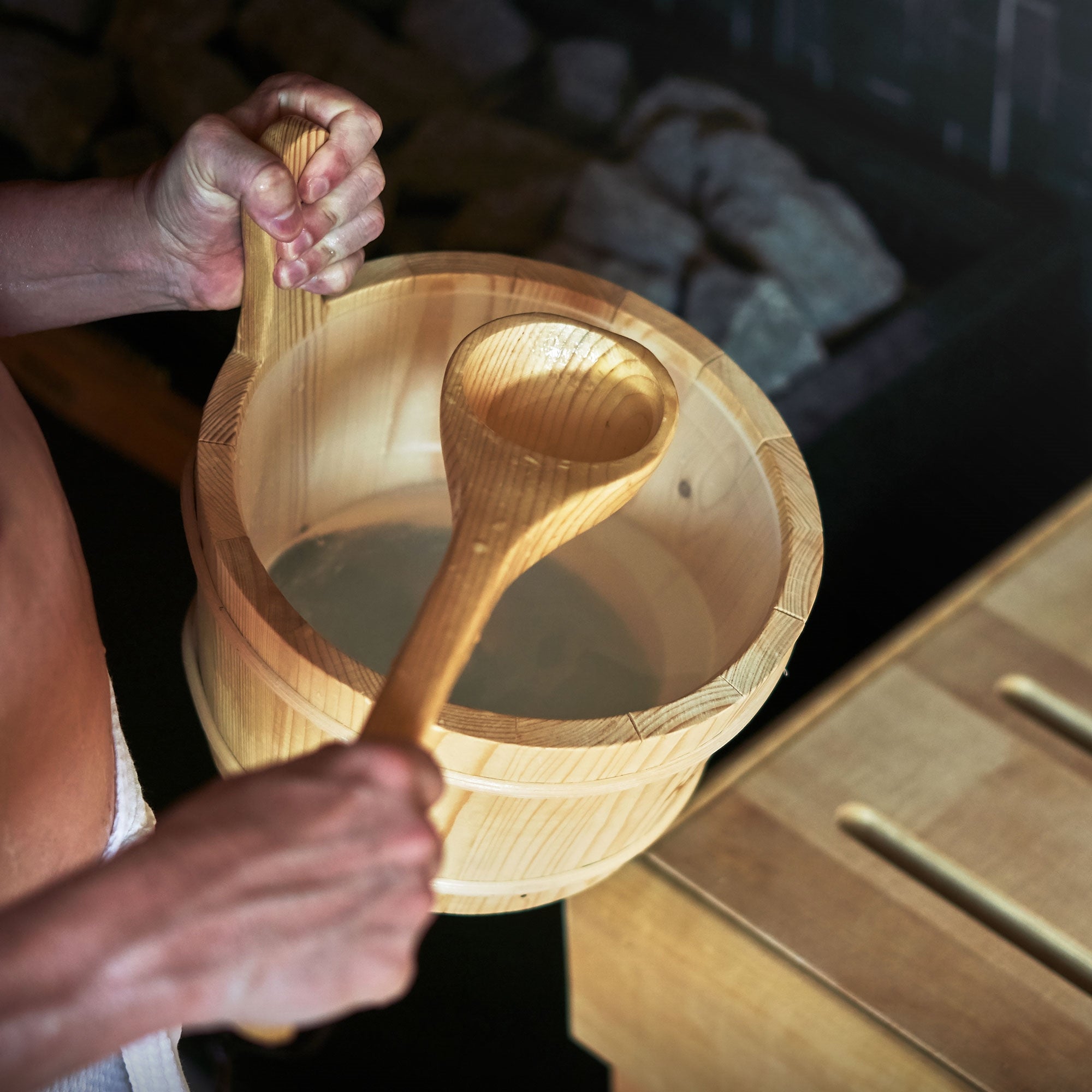 Eine Person hält einen Eimer mit Wasser und eine Schöpfkelle in der Sauna.