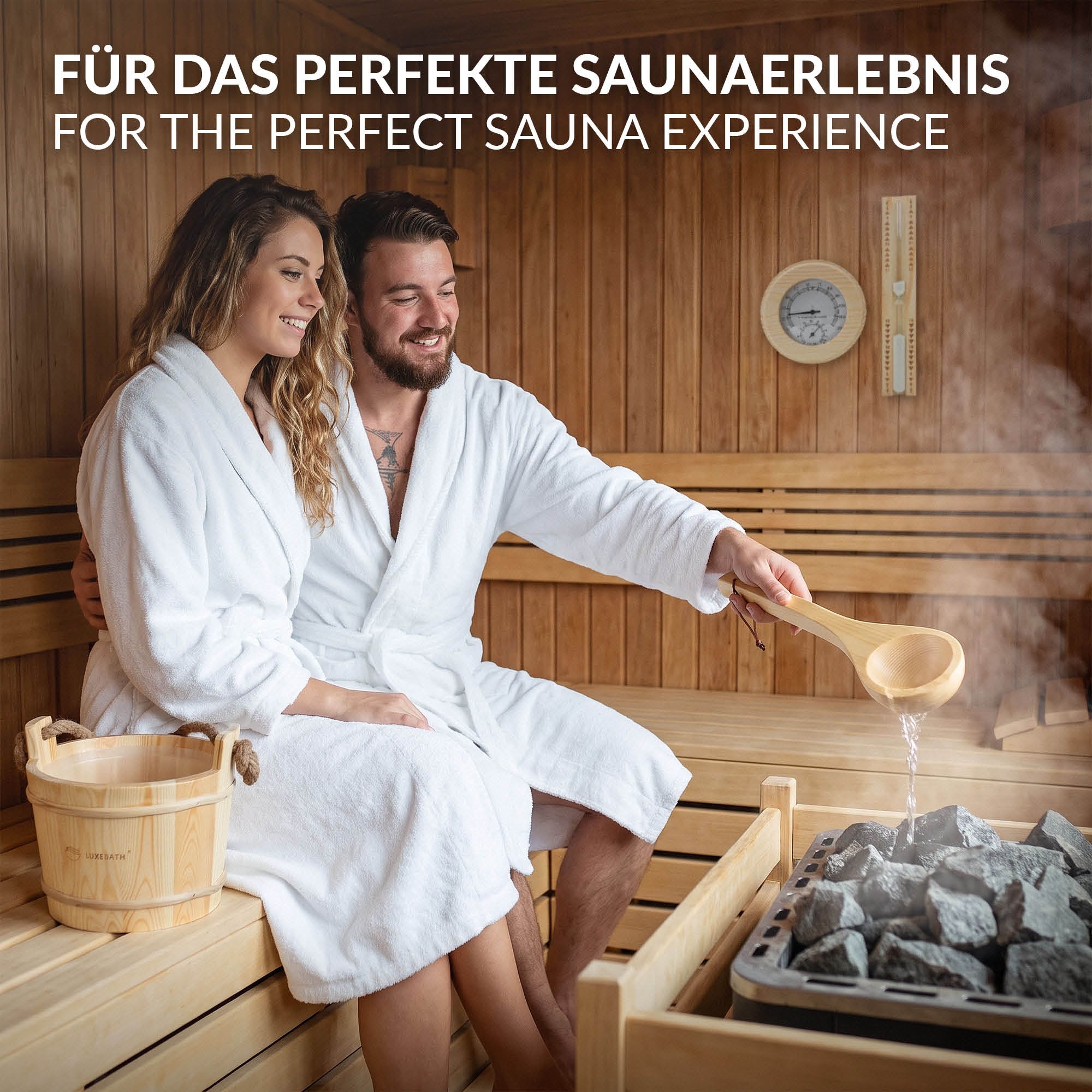 Paar in Bademänteln sitzt in einer Sauna, Holzofen im Hintergrund, Wasserschaufel in der Hand.