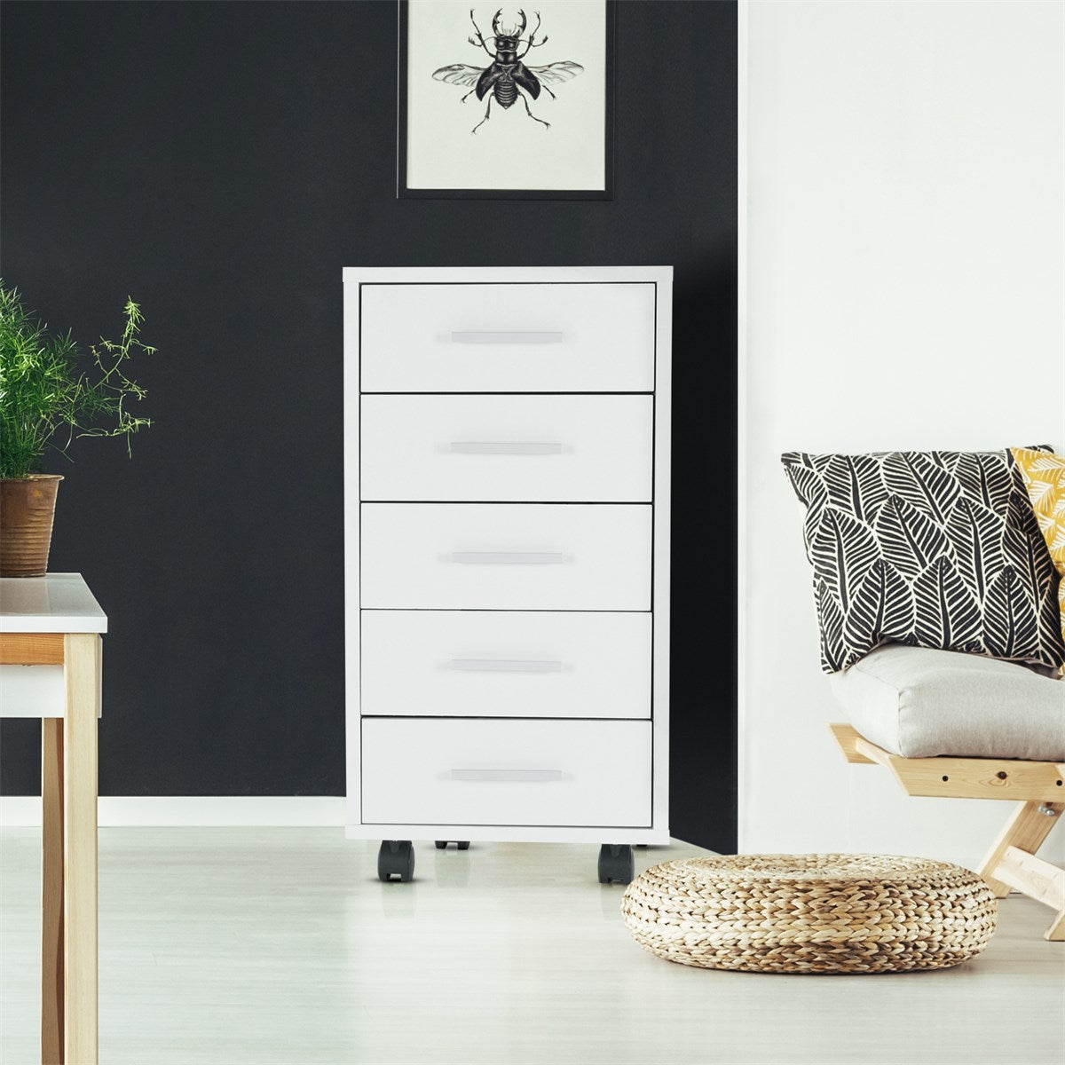 White chest of drawers with five drawers, a plant and a chair in the background.
