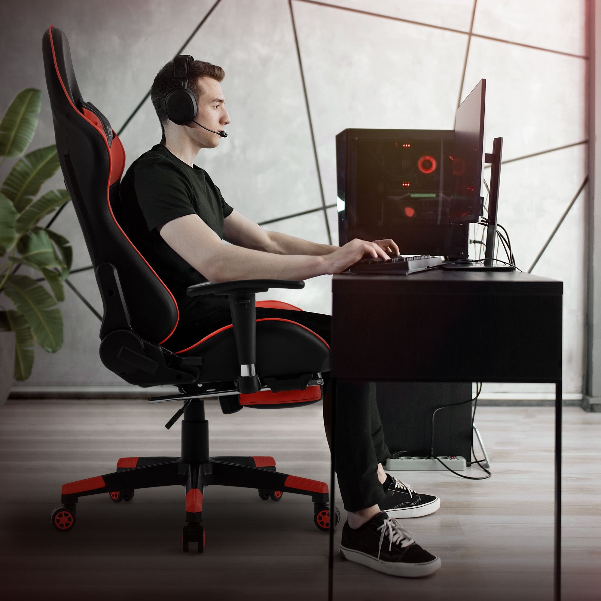 Junger Mann sitzt an einem Schreibtisch mit Gaming-Stuhl und Computer.