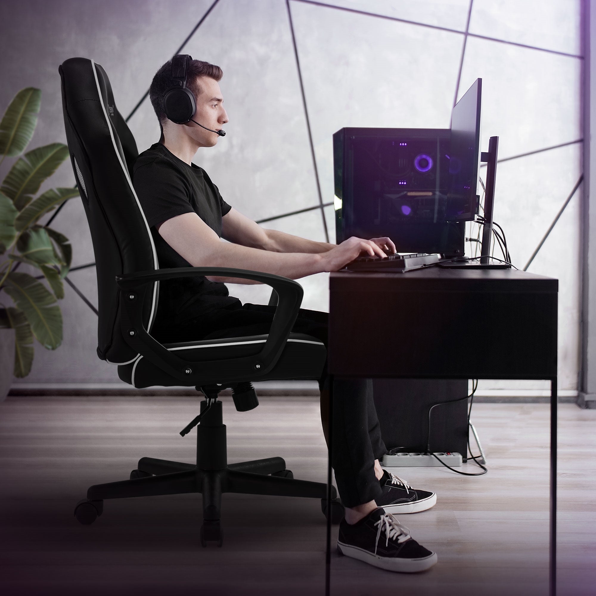 Man sitting at a desk with headset and computer, surrounded by plants.