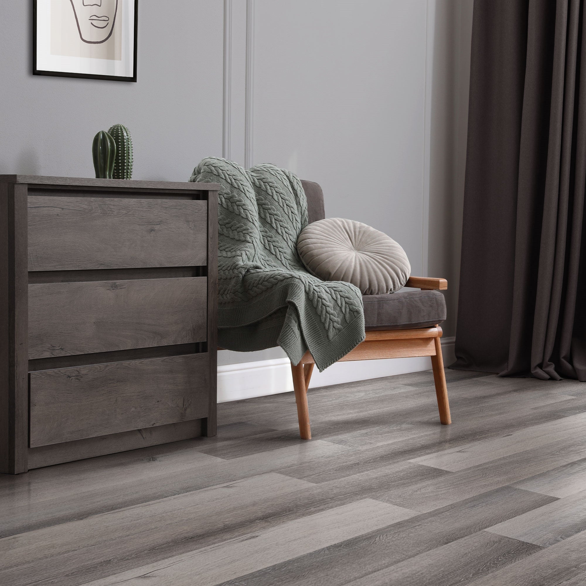 Ein graues Sofa mit einer Decke, Kissen und einem Schrank im Hintergrund.