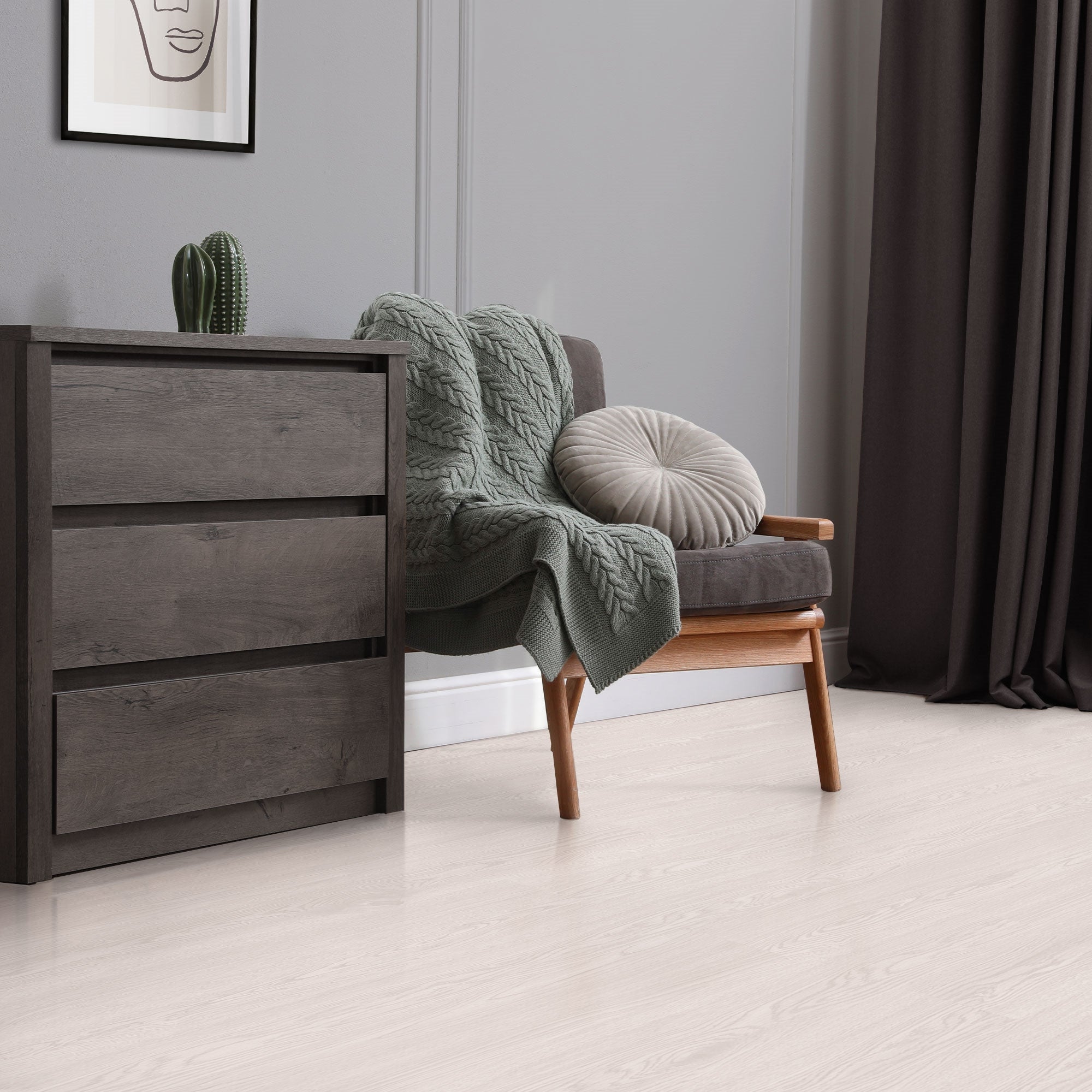 Nojatuoli peiton ja tyynyn kanssa komodin edessä.